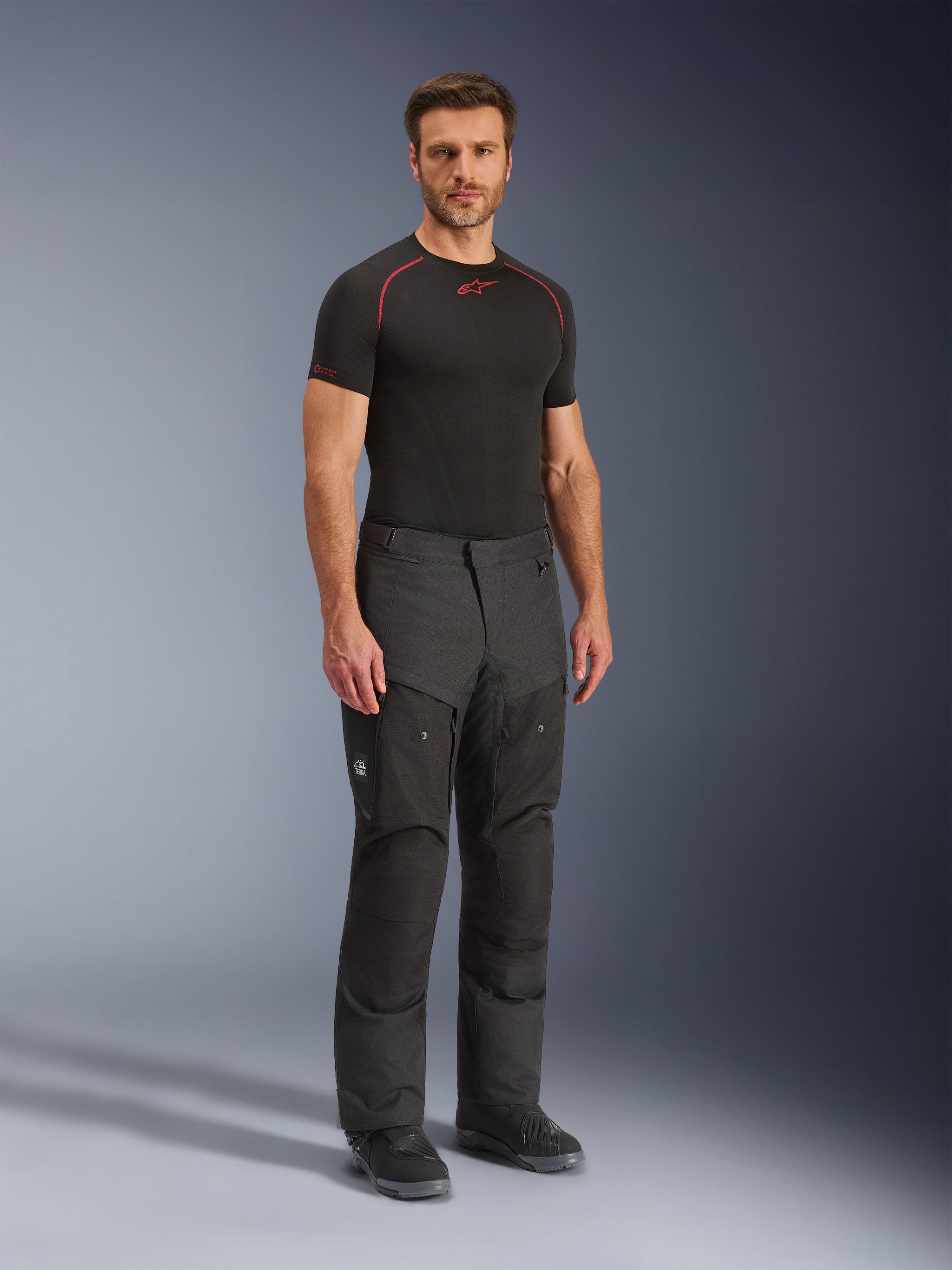 Alpinestars Cusco Drystar® Pants, Black textile motorcycle pants, worn by a model with a black base layer and boots, featuring ripstop fabric, large cargo pockets with 'Terra' branding, and ergonomic design for adventure riding.