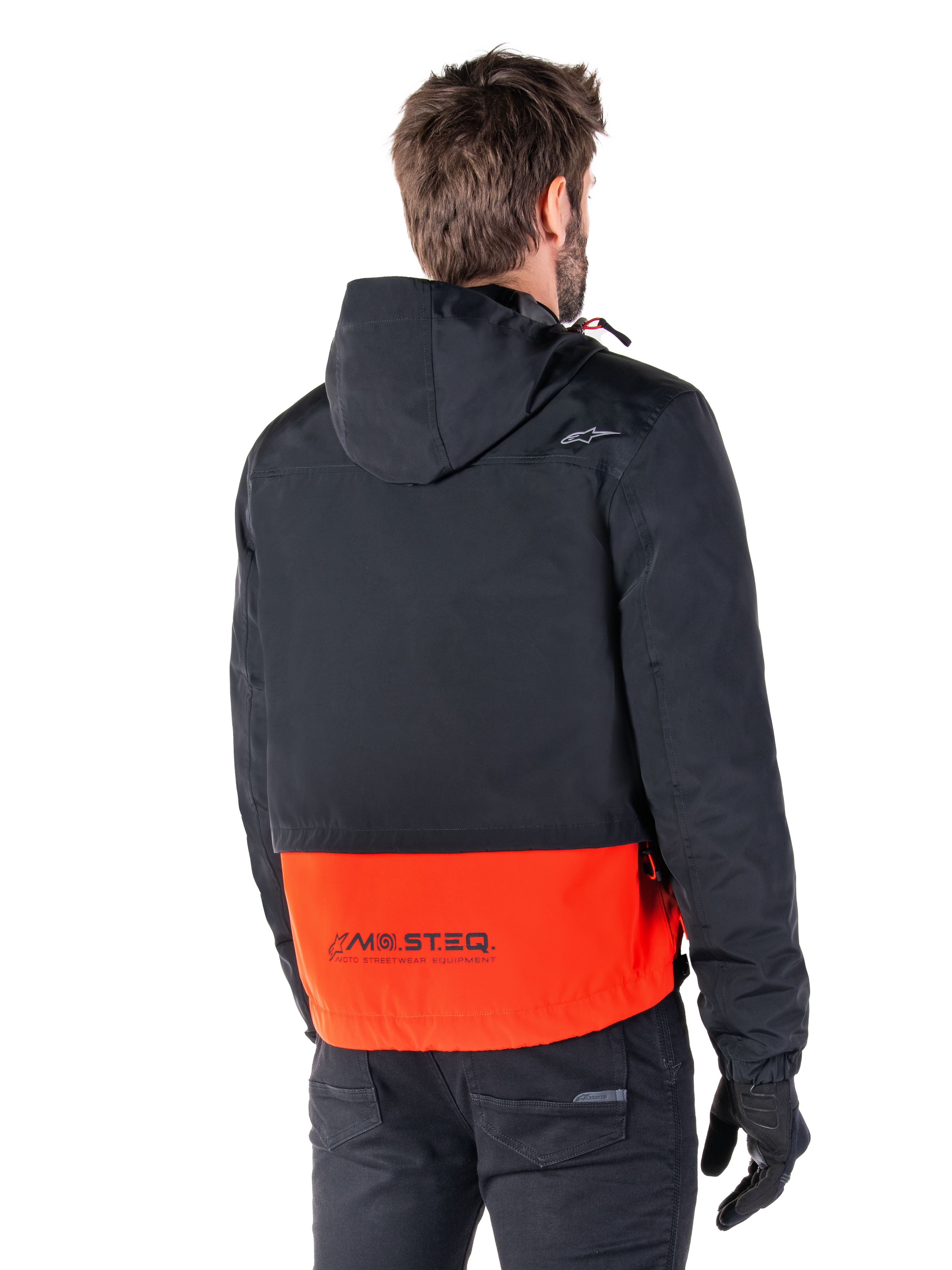 Alpinestars Mootant Waterproof Parka, Spicy Orange and Black, rear view on a male model, features a hooded black upper and bright orange lower section with MO.ST.EQ. branding, urban contemporary motorcycle jacket worn with black pants and gloves