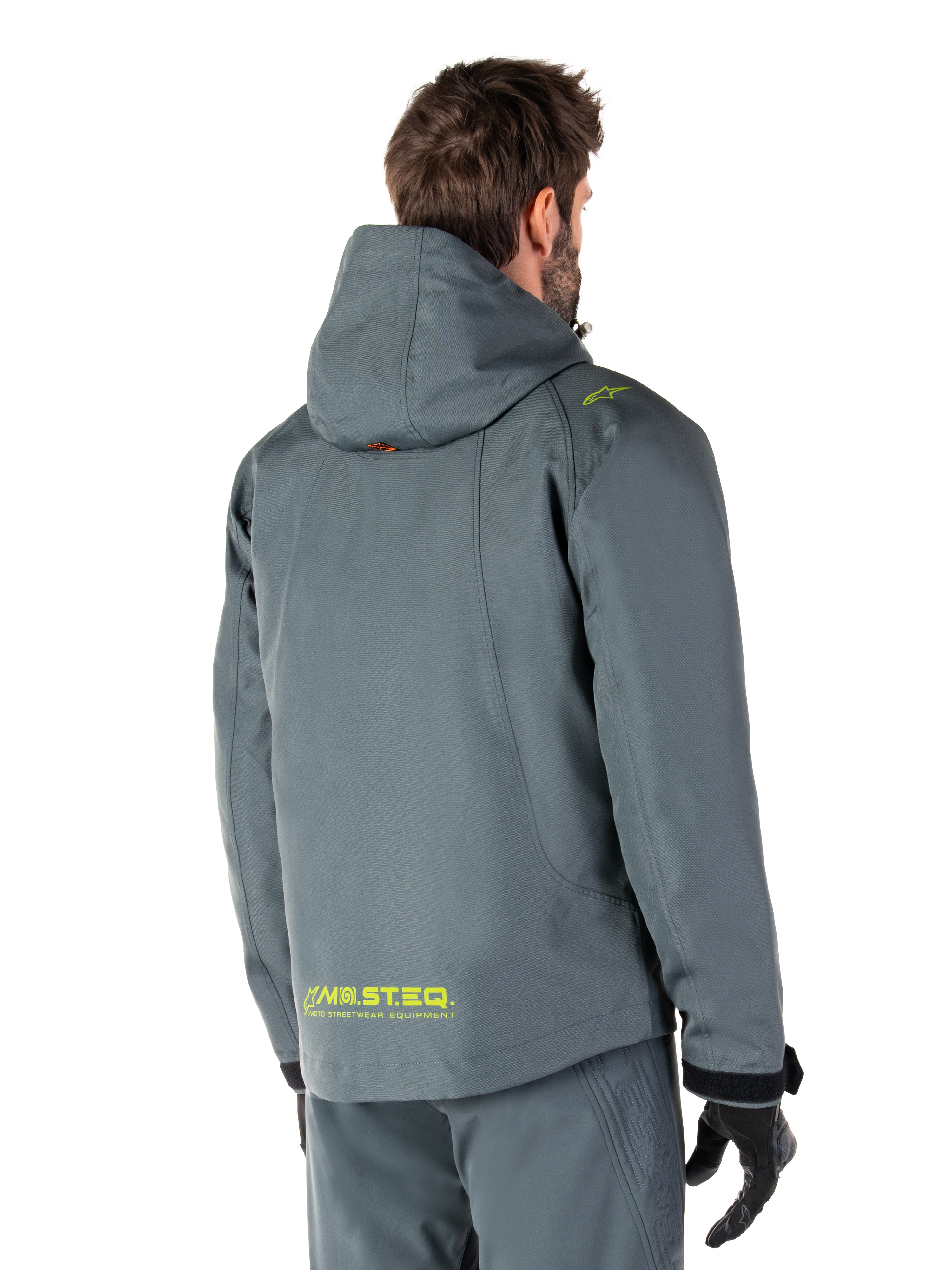 Alpinestars Morush Waterproof Parka in Urban Gray, rear view, featuring yellow MO.ST.EQ. branding on the lower back and shoulder, minimalist hooded design, worn with matching gray riding pants and black gloves, urban motorcycle streetwear.