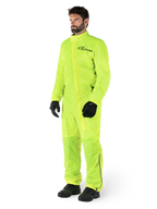 Alpinestars Hurricane Rain V2 Suit, One-piece waterproof motorcycle suit, Yellow Fluo, worn with black gloves and boots, featuring a black Alpinestars logo on the chest and reflective detailing on the legs