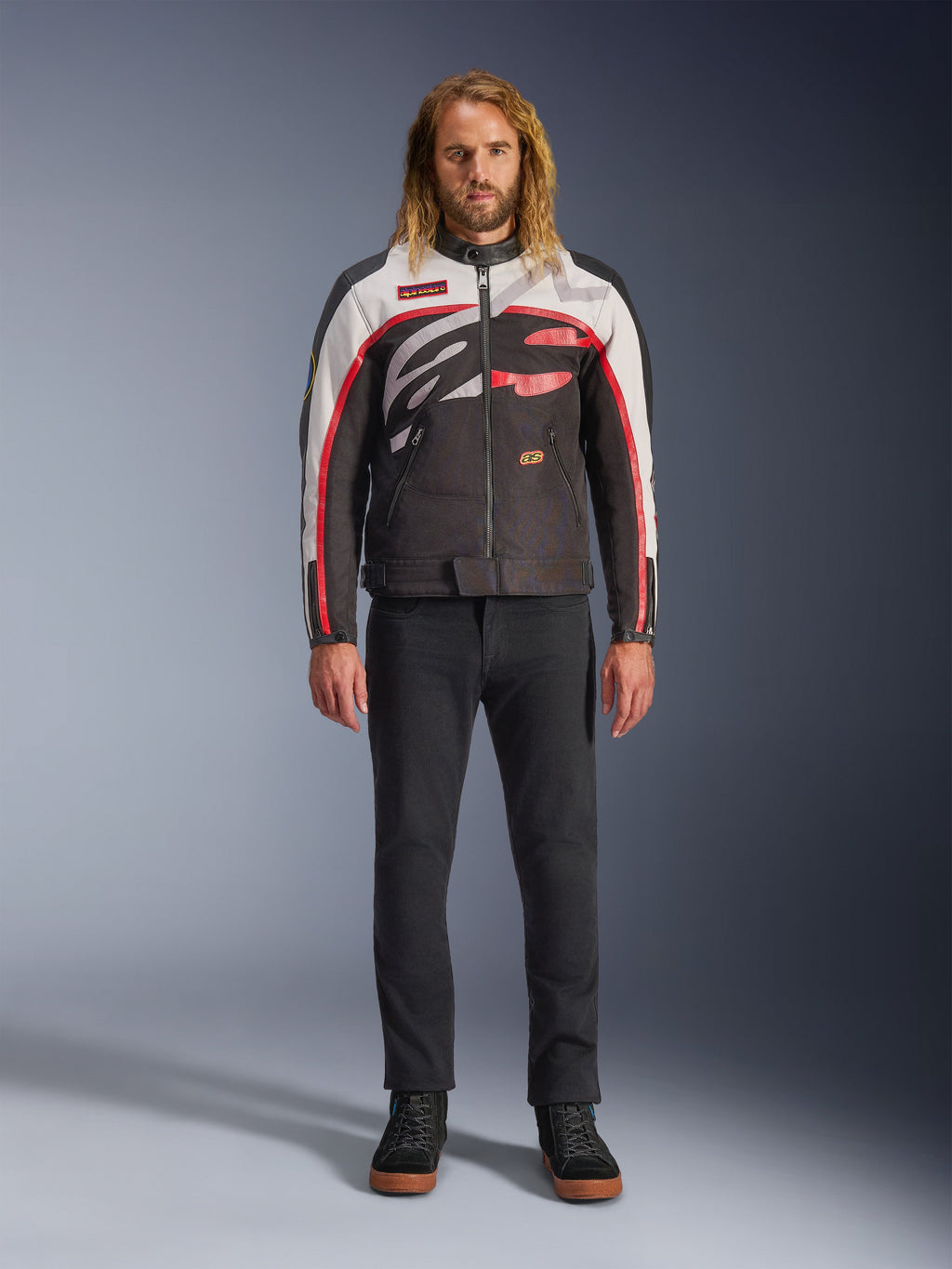 Alpinestars Axton Jacket, Motorcycle Jacket, Black Off White and Bright Red, worn by a model with black pants and sneakers, featuring a bold wrap-around logo and vintage racing-inspired design