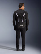 Alpinestars AST V3 Air Jacket, Back View, Black and Dark Gray with White accents, featuring large white Astar logo on the tail, reflective stripes on the back, and mesh textile construction, worn with black pants and boots for a sport riding look