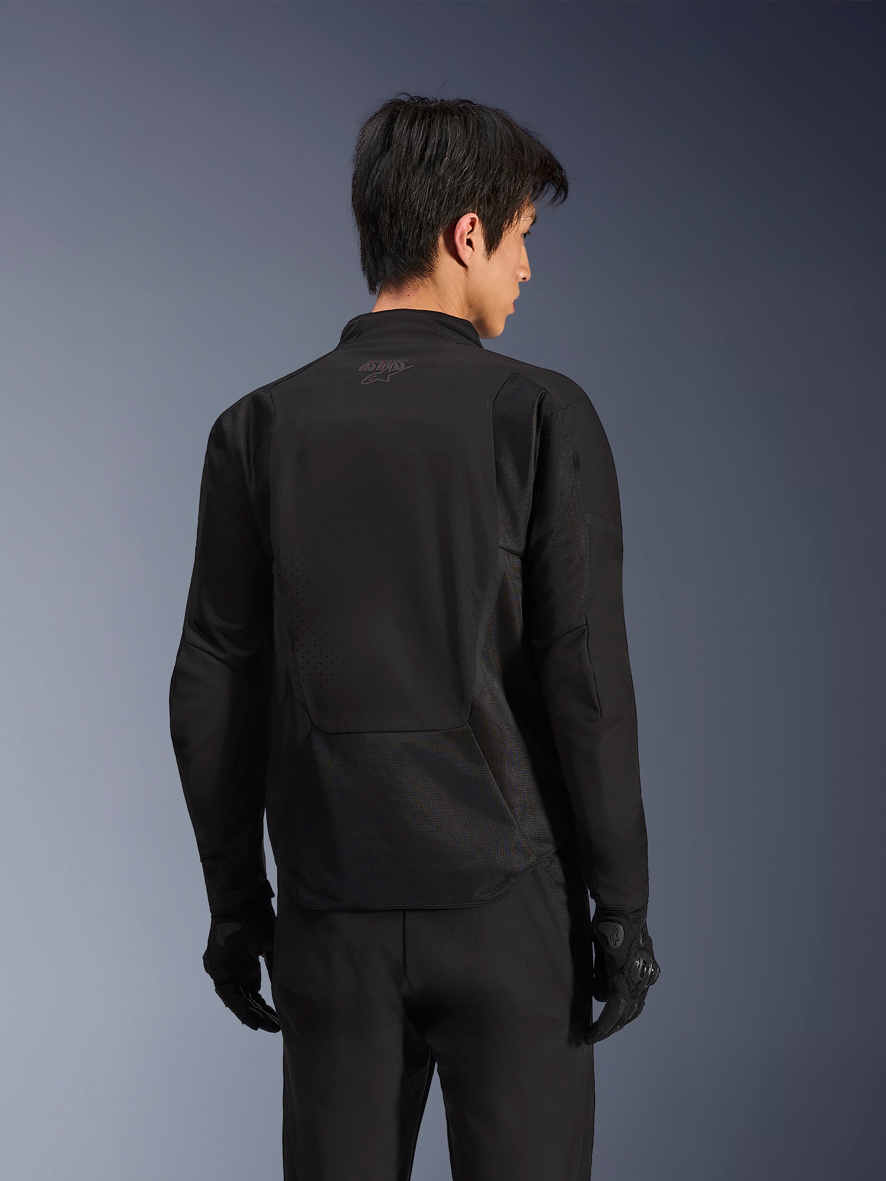 Alpinestars Aeroshell Airflow Jacket, Black Anthracite, back view of sport motorcycle jacket featuring laser-perforated ventilation zones and 2D mesh panels, elongated rear for coverage, worn with black riding gloves