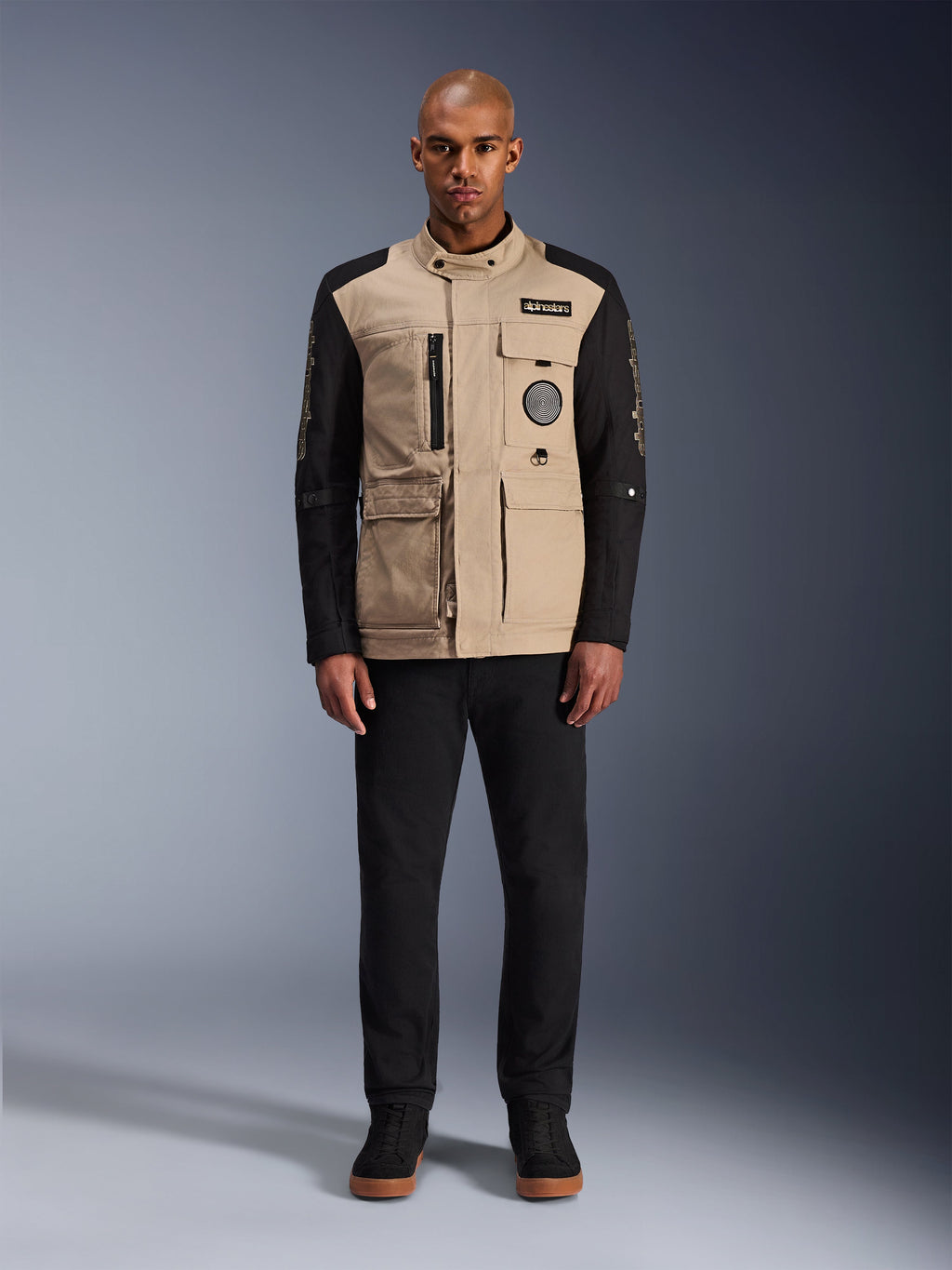 Alpinestars Dice Jacket, urban motorcycle jacket, aluminum tan body with black sleeves, workwear-inspired silhouette with four front utility pockets, worn with black pants and black high-top sneakers, rugged street-ready riding gear