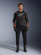 Male model wearing Alpinestars T-SPS Air v2 Jacket, Black textile motorcycle jacket with Red Fluo accents, white logo on chest, worn with black pants, gloves and boots, urban sport riding style