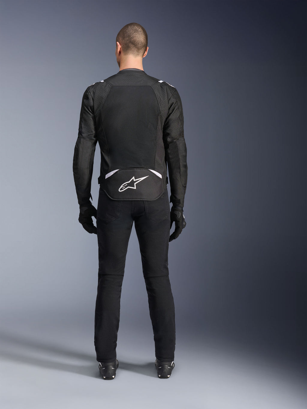 Alpinestars T-Sps Air V2 Jacket, Rear View, Black and White textile motorcycle jacket, featuring a large mesh back panel for maximum airflow and white Astars logo on the lower back, worn with black riding pants and gloves