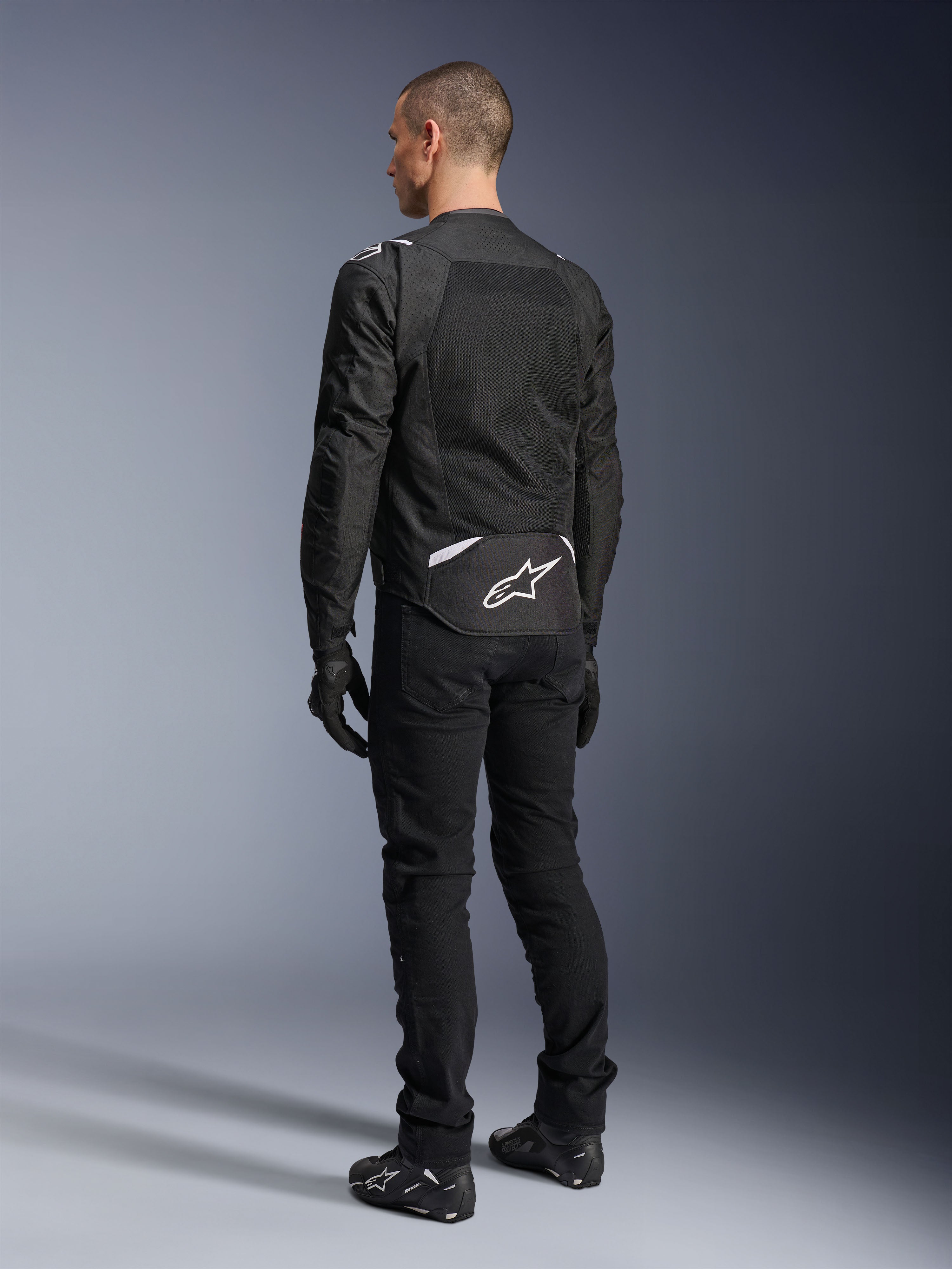 Alpinestars T-Sps Air V2 Jacket, Textile Motorcycle Jacket, Black, rear view showing large mesh ventilation panel and white Alpinestars logo on the lower back, paired with black riding pants and gloves for a sporty urban look.