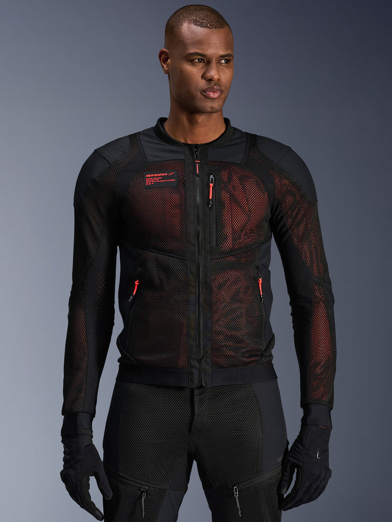 Alpinestars Troop-Air Pro Jacket, technical armored mesh motorcycle jacket in Black and Red Fluo, worn by a model, featuring large mesh ventilation panels, red underlay, and red zipper pulls, urban riding style.