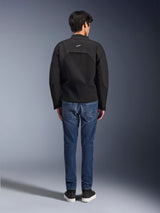 Rear view of a model wearing the Alpinestars Provoke Jacket, black technical textile motorcycle jacket, styled with blue denim riding jeans and black sneakers, showing the back construction and small white Alpinestars logo, urban contemporary design