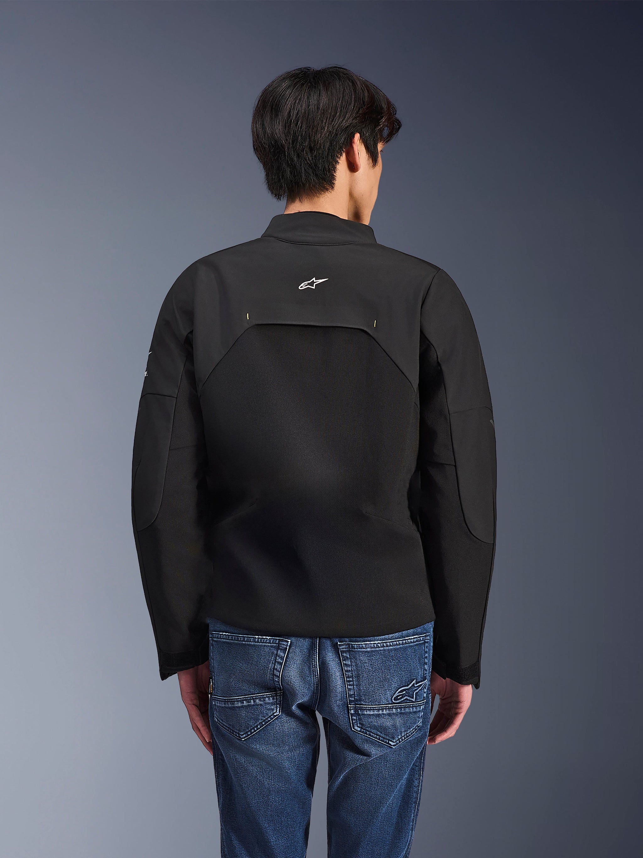 Alpinestars Provoke Jacket, Urban Motorcycle Jacket, Black, rear view showing white Astars logo and technical ripstop panels, worn with blue denim jeans, contemporary design for city commuting