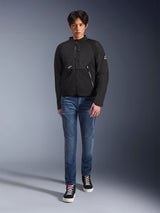 Male model wearing Alpinestars Provoke Jacket in Black, urban textile motorcycle jacket featuring technical zippers and ripstop softshell panels, paired with blue jeans and black sneakers, contemporary urban rider style.