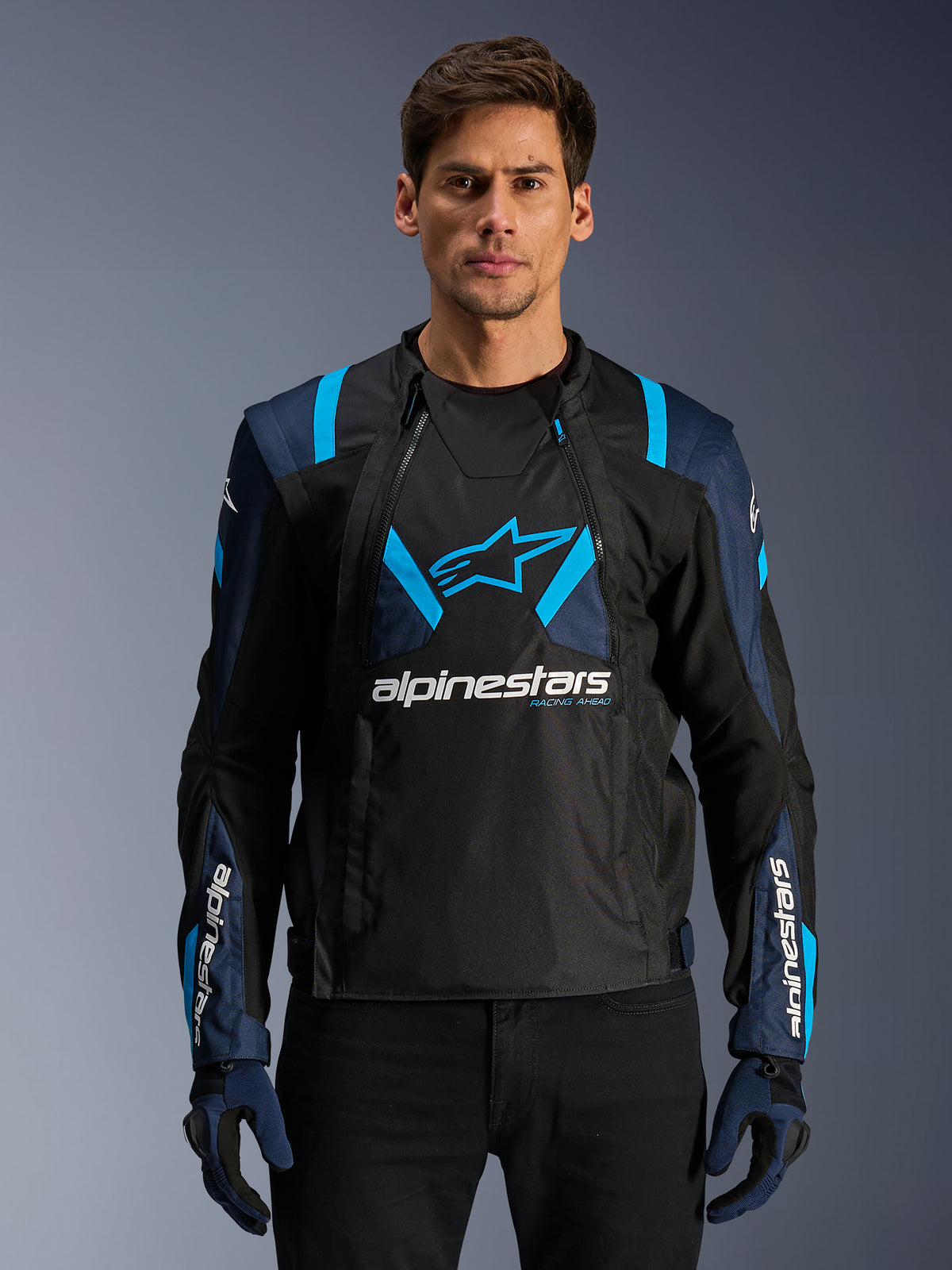 Alpinestars T-Stunt Air Jacket, Motorcycle Mesh Jacket, Black and Blue, worn by a model with black pants and gloves, featuring a modular 2-in-1 design with breathable tech mesh panels, star logo on the chest, and Alpinestars branding on the sleeves.