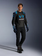 Male model wearing Alpinestars T-Stunt Air Jacket, Black Dark Blue and Blithe Blue, featuring prominent mesh panels for airflow, paired with black pants and riding gloves, sport-cut motorcycle jacket for summer road riding.