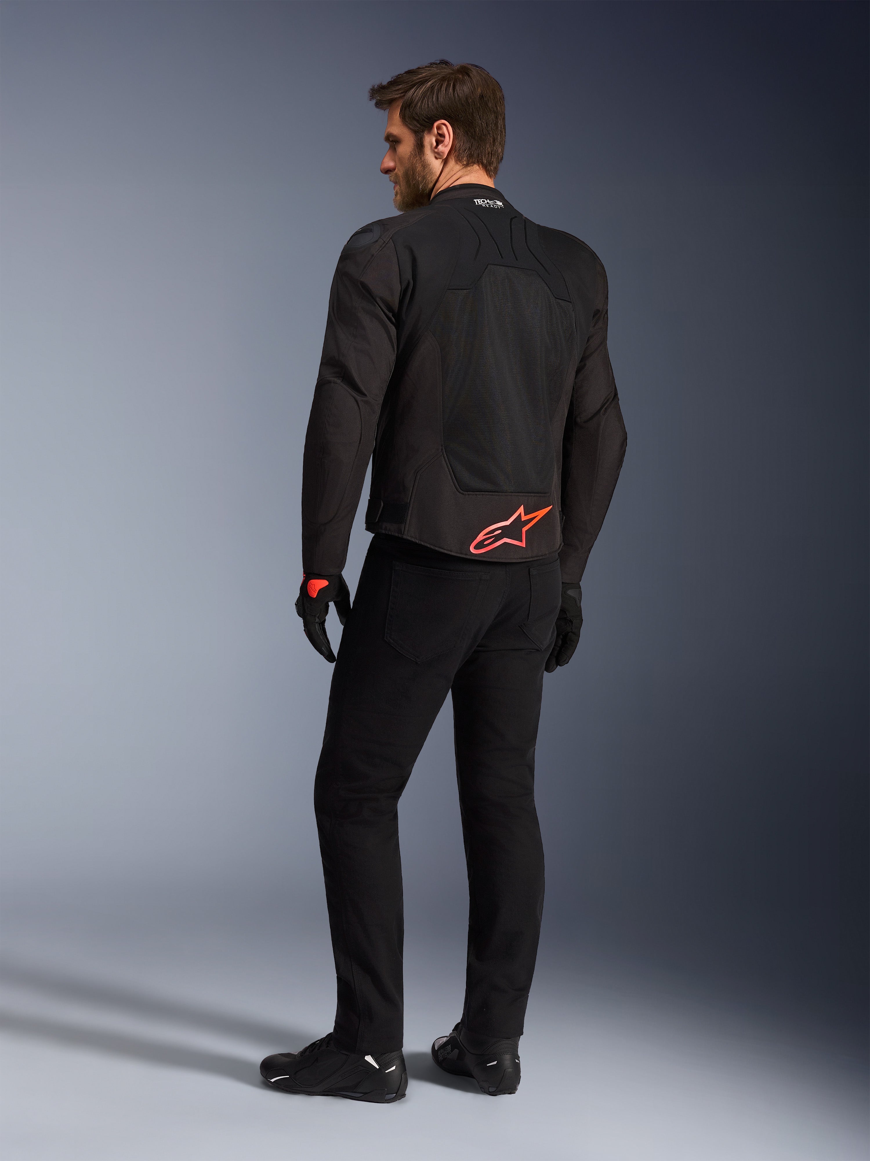 Rear view of a model wearing the Alpinestars SMX Air Jacket in Black, featuring a bright red Alpinestars logo on the lower back, 'Tech-Air Ready' branding on the collar, and technical mesh panels for ventilation, paired with black riding pants and gloves.