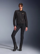 Woman wearing the Alpinestars Stella Grace Jacket in Black, urban motorcycle jacket with workwear aesthetics, featuring front zippered pockets and chest logo, paired with slim-fit black pants and black boots, contemporary women's riding gear.