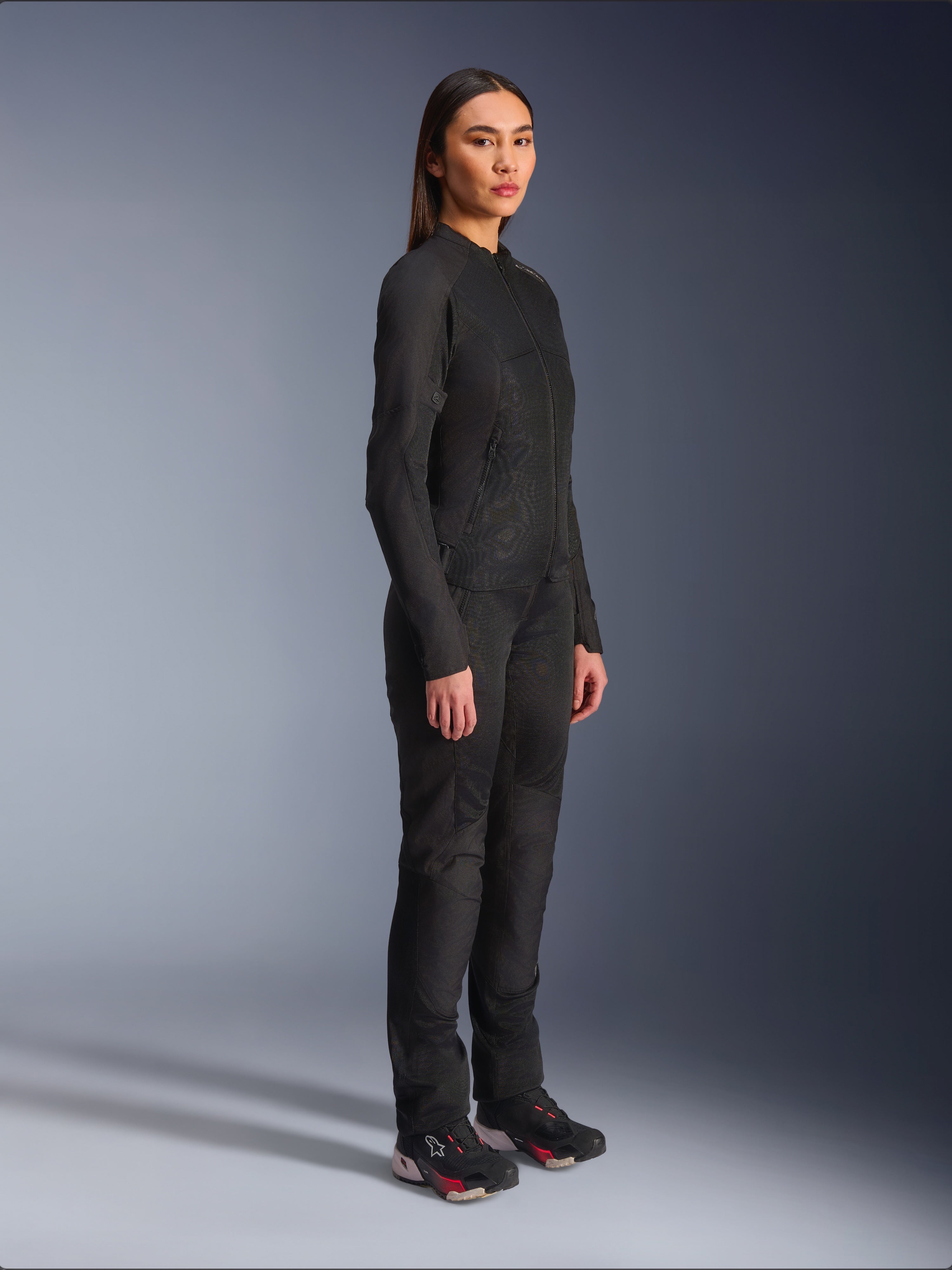 Alpinestars Woman Stella C-1 Air Jacket in Black, textile motorcycle jacket with mesh panels, worn with matching black riding pants and technical sneakers, studio shot showing a full-length urban riding outfit.