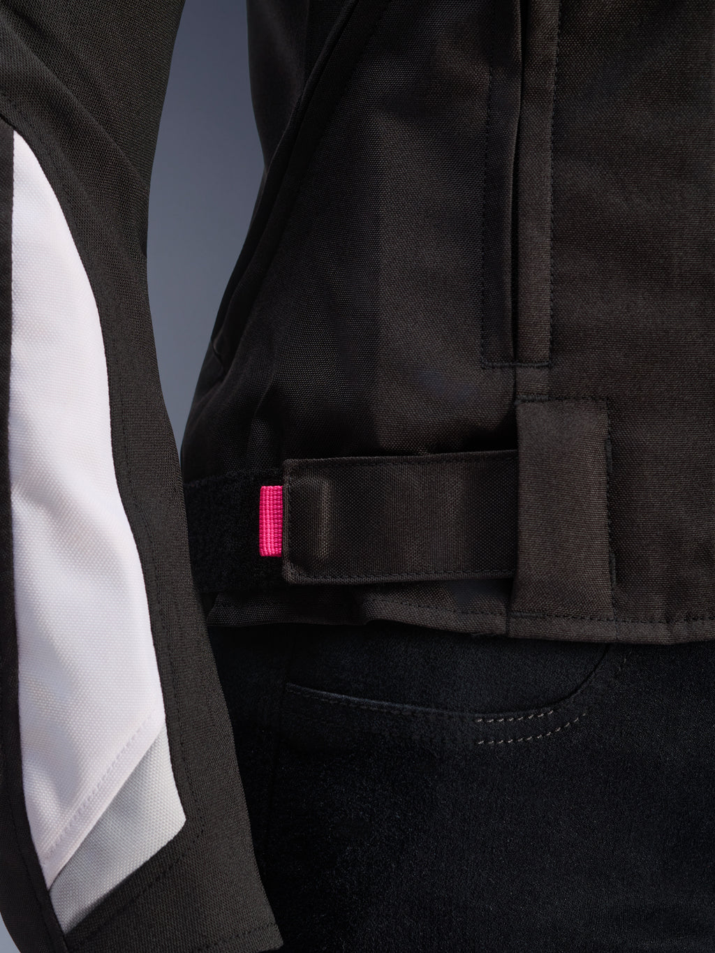 Alpinestars Stella T-GP Plus R V4 Jacket, Black and White, close-up of the adjustable waist strap with pink accent tab, durable textile construction with white sleeve paneling, sport-fit women's motorcycle jacket.