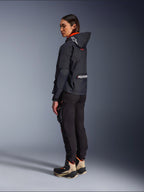 Female rider wearing the Alpinestars Molly Air Jacket in Black Fluo Coral, rear side view showing the hood with Astars logo and large Alpinestars branding on the back, paired with black cargo riding pants and tan and black adventure boots, contemporary urban motorcycle gear for women