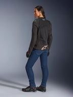 Alpinestars Stella SMX Air Jacket, Black with white and red logo, worn by a female rider seen from a rear three-quarter view, styled with blue motorcycle jeans and black riding footwear, featuring technical mesh construction for warm-weather sport riding.