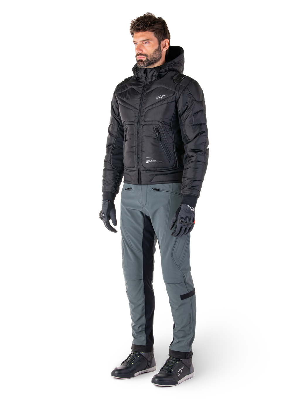 Alpinestars Alden Pants in Urban Gray, worn by a model with a black quilted hooded jacket, gloves, and riding shoes, featuring quilted detailing on the sides and black inner leg panels, streetwear-inspired urban motorcycle gear.