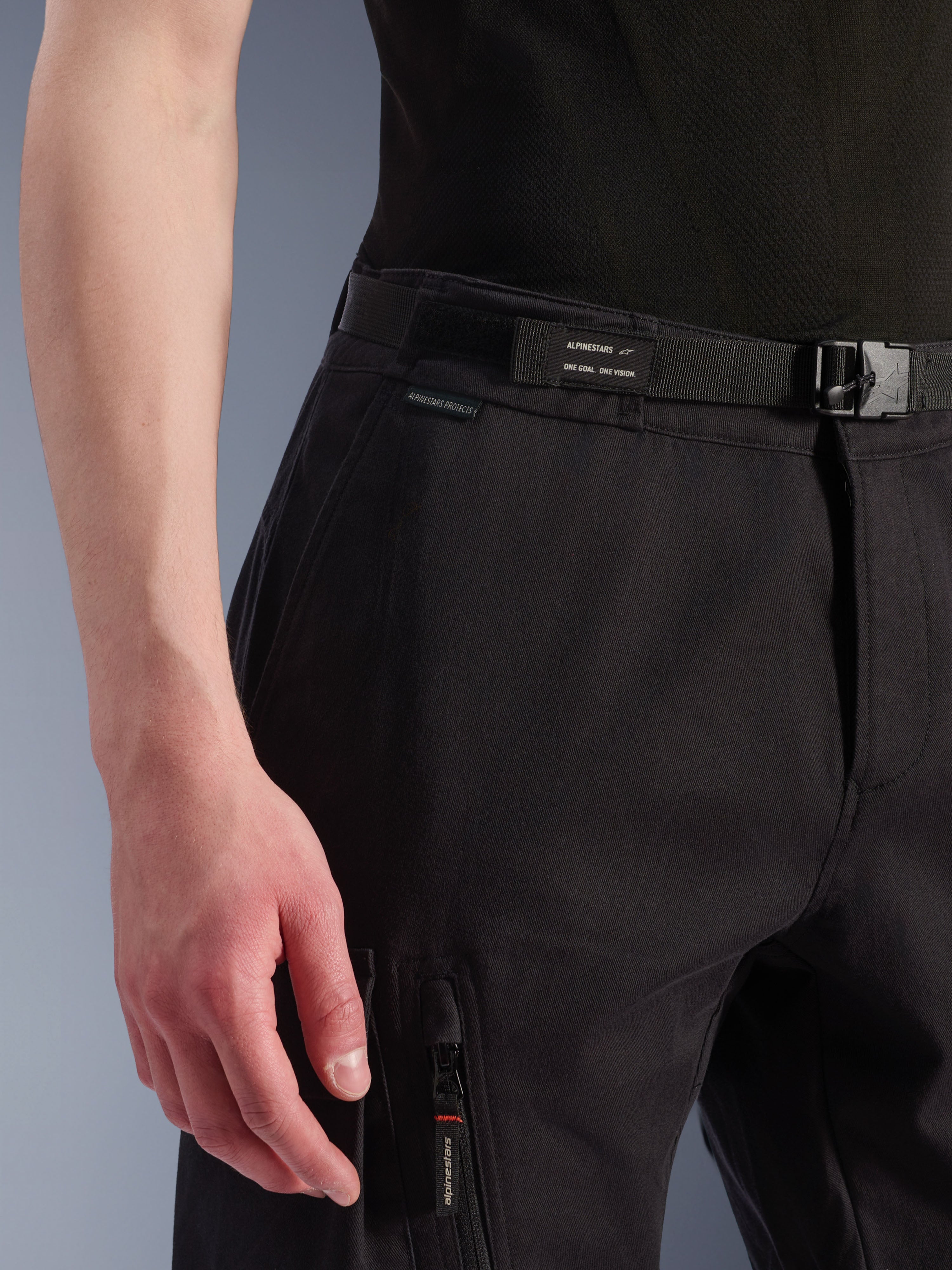 Alpinestars Flex-AST Cargo Pants, Black, close-up of waist and hip area, featuring an integrated adjustable belt with Alpinestars branding, buckle closure, and a zippered cargo pocket, technical stretch fabric for urban motorcycle gear