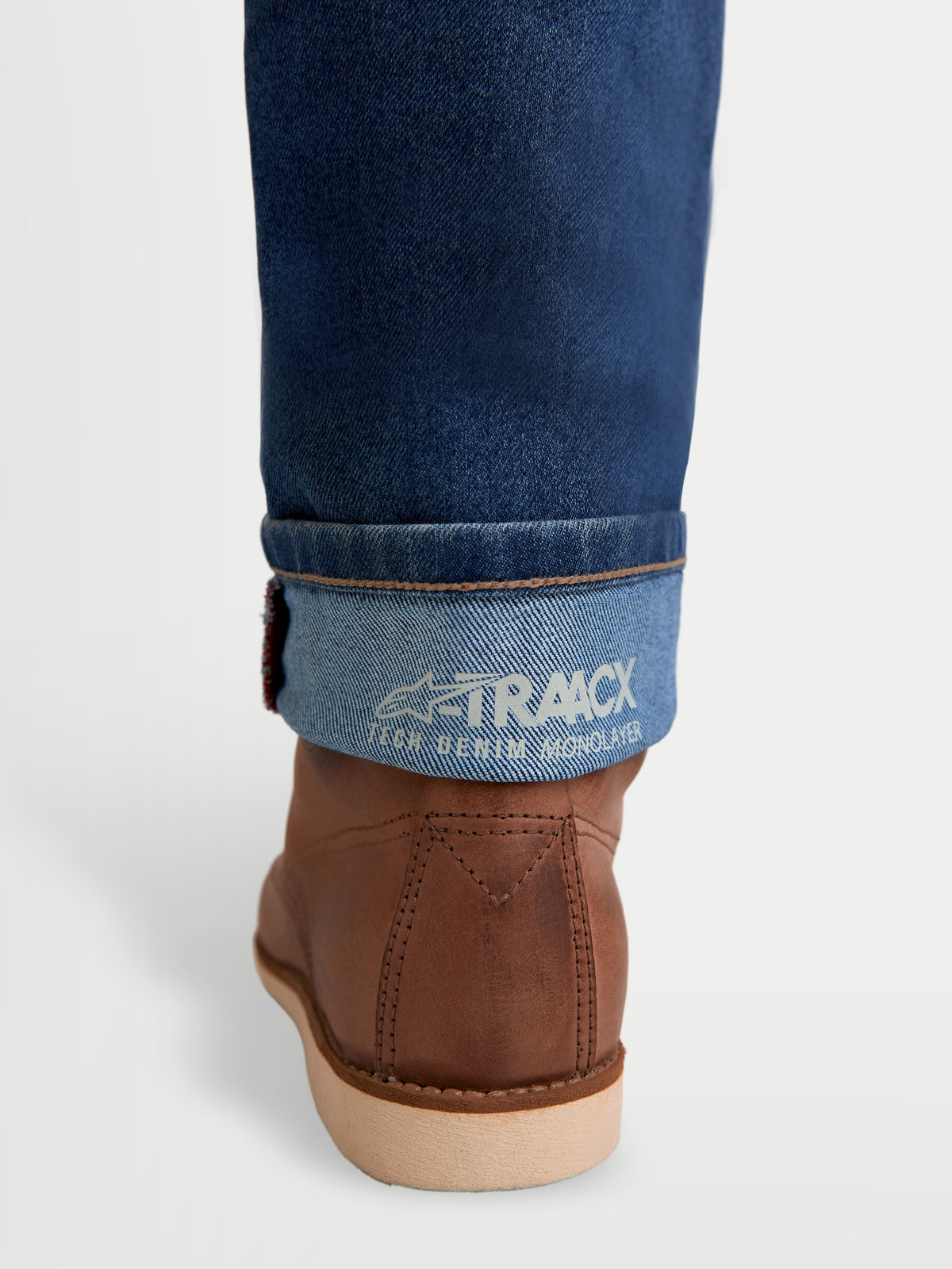 Alpinestars Flex-AST 7 Denim Pants, men's urban motorcycle riding jeans, light blue, detailed view of rolled cuff showing A-TRAACX tech denim monolayer branding and brown leather riding boots