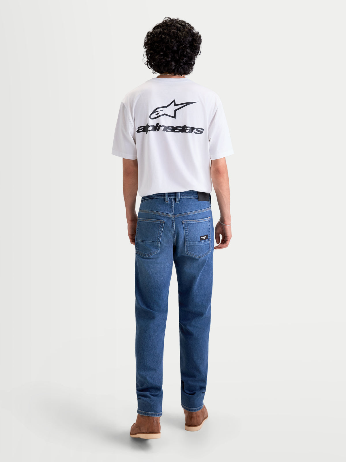 Alpinestars Flex-AST 7 Denim Pants, men's urban contemporary motorcycle riding jeans in light blue, rear view on a model wearing a white t-shirt, showing single-layer AA-rated technical denim and a five-pocket layout with back patch detail.