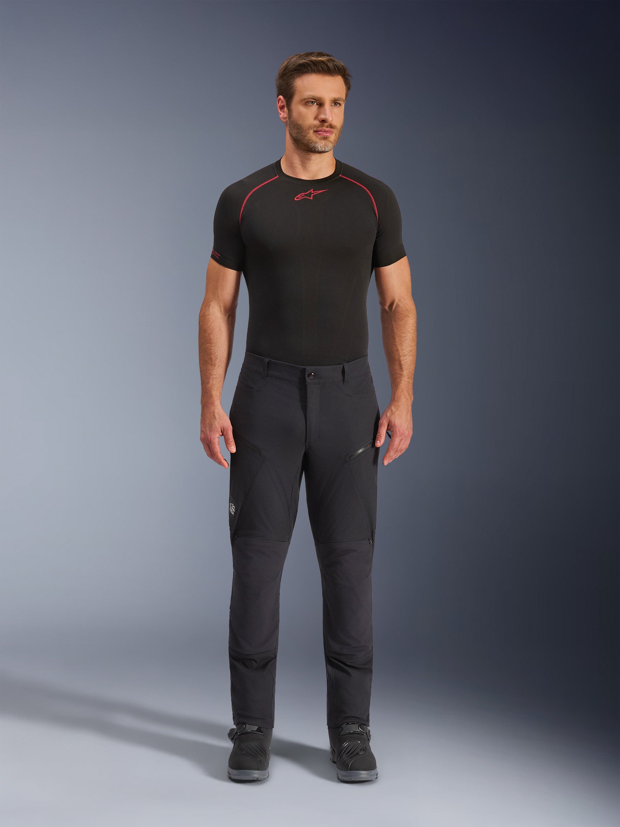 Alpinestars Flex-AST Explorer Pants, Black adventure touring motorcycle pants, man wearing fitted textile riding pants with zippered cargo pockets and reinforced panels, styled with a black base layer and motorcycle boots, durable protection for adventure riding