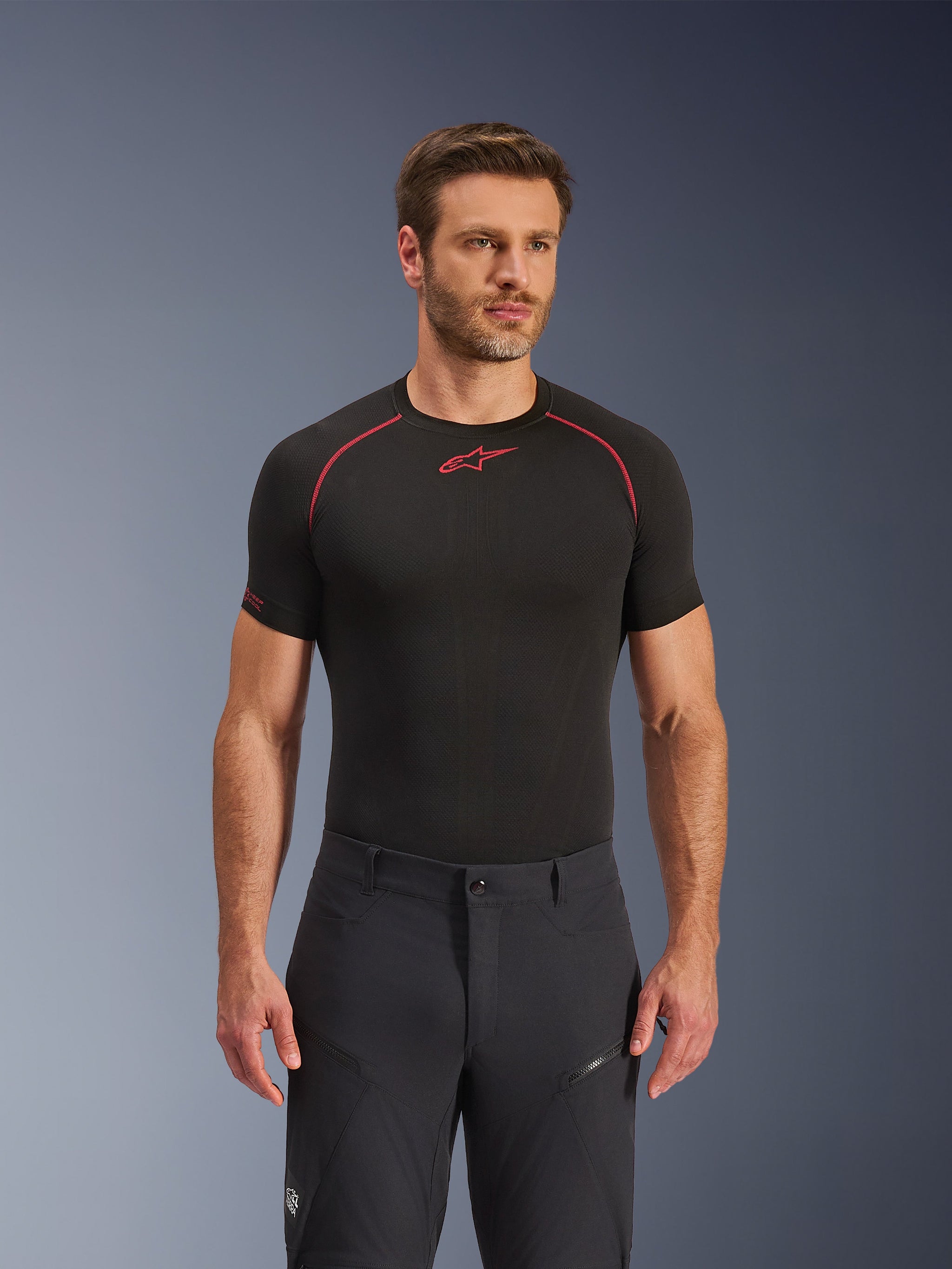 Alpinestars Flex-AST Explorer Pants, Black, adventure motorcycle pants worn with a black short-sleeve base layer featuring red stitching, technical textile construction with zippered pockets and belt loops, studio portrait.