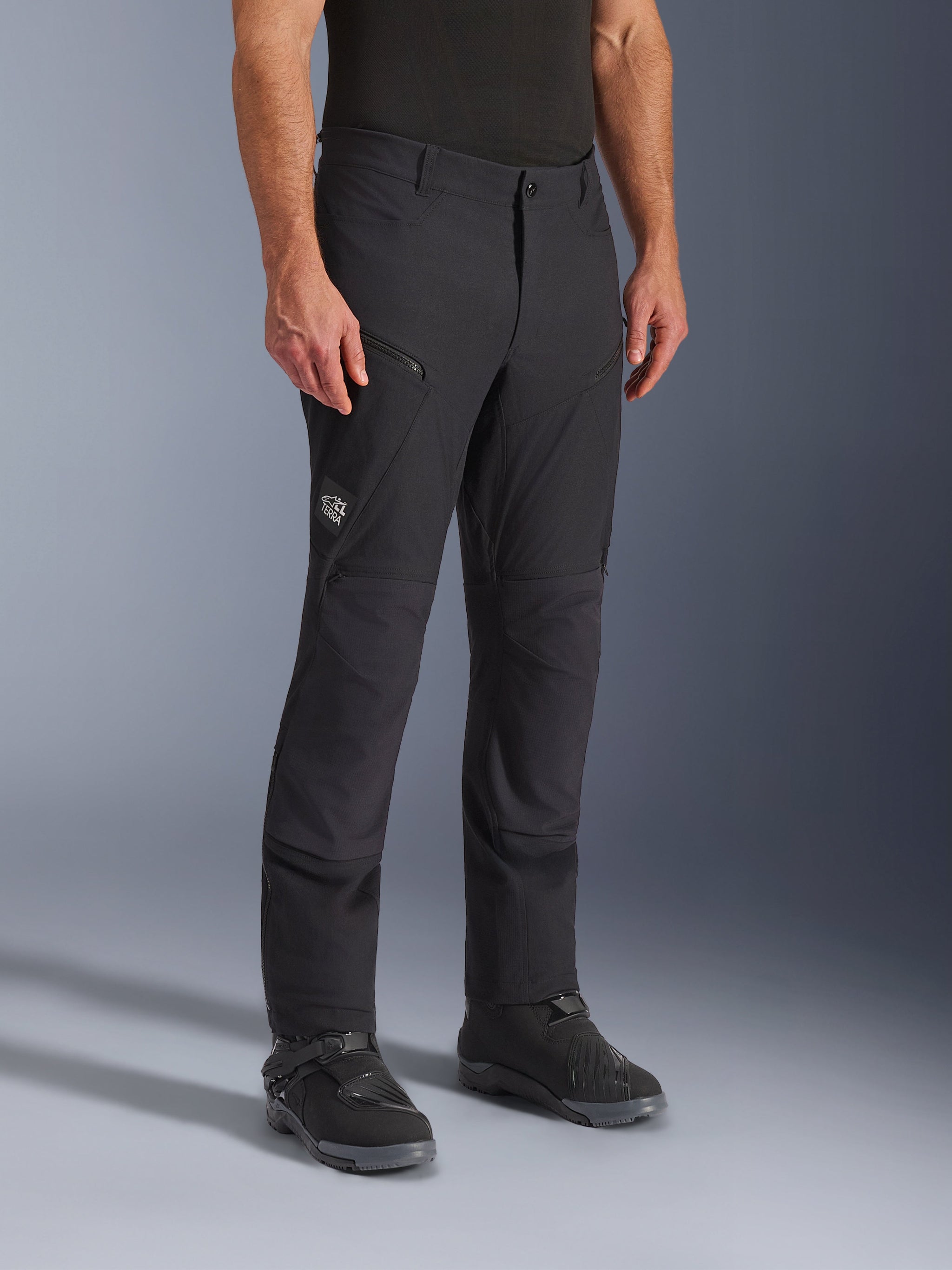 Alpinestars Explore AST Pants Short, Black Adventure Motorcycle Pants, stretch ripstop construction, featuring zippered cargo pockets and subtle 'All Terra' branding on the thigh, worn with black riding shoes, designed for warm-weather touring and adventure riding.