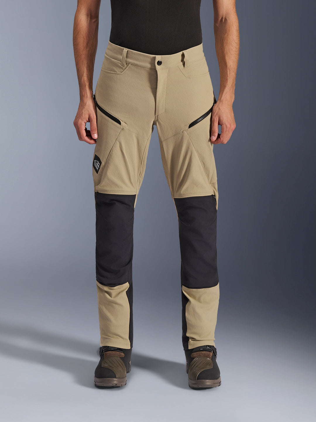 Alpinestars Flex-AST Explorer Pants, Adventure Motorcycle Pants, Tan and Black, featuring ripstop knee reinforcements, diagonal zippered pockets, and ALL TERRA branding on the thigh, front view on model