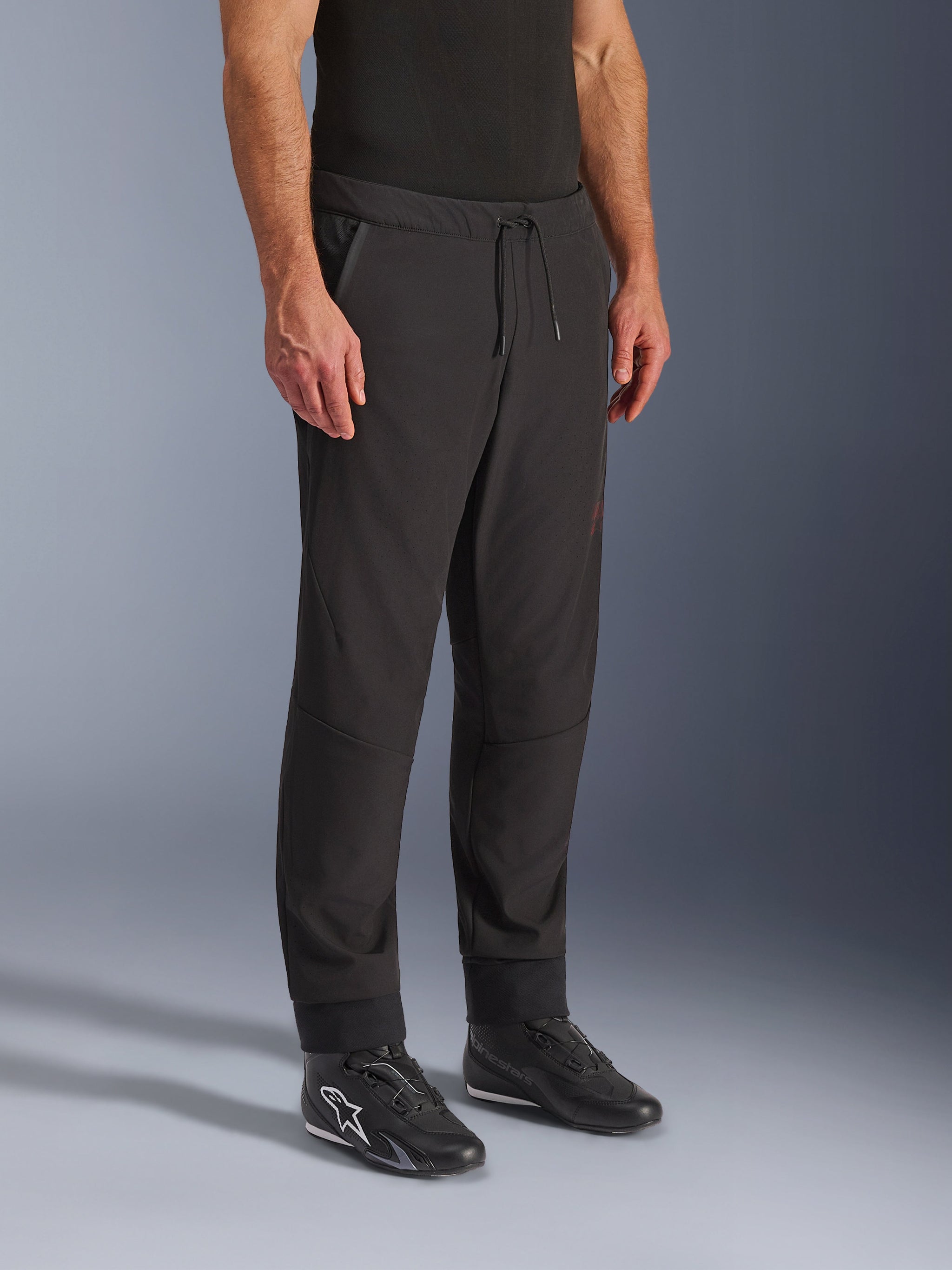 Alpinestars Aeroshell Airflow Pants, Black Motorcycle Pants, worn by model with black riding shoes, featuring a drawstring waistband, cuffed ankles, and laser-perforated softshell fabric for maximum ventilation