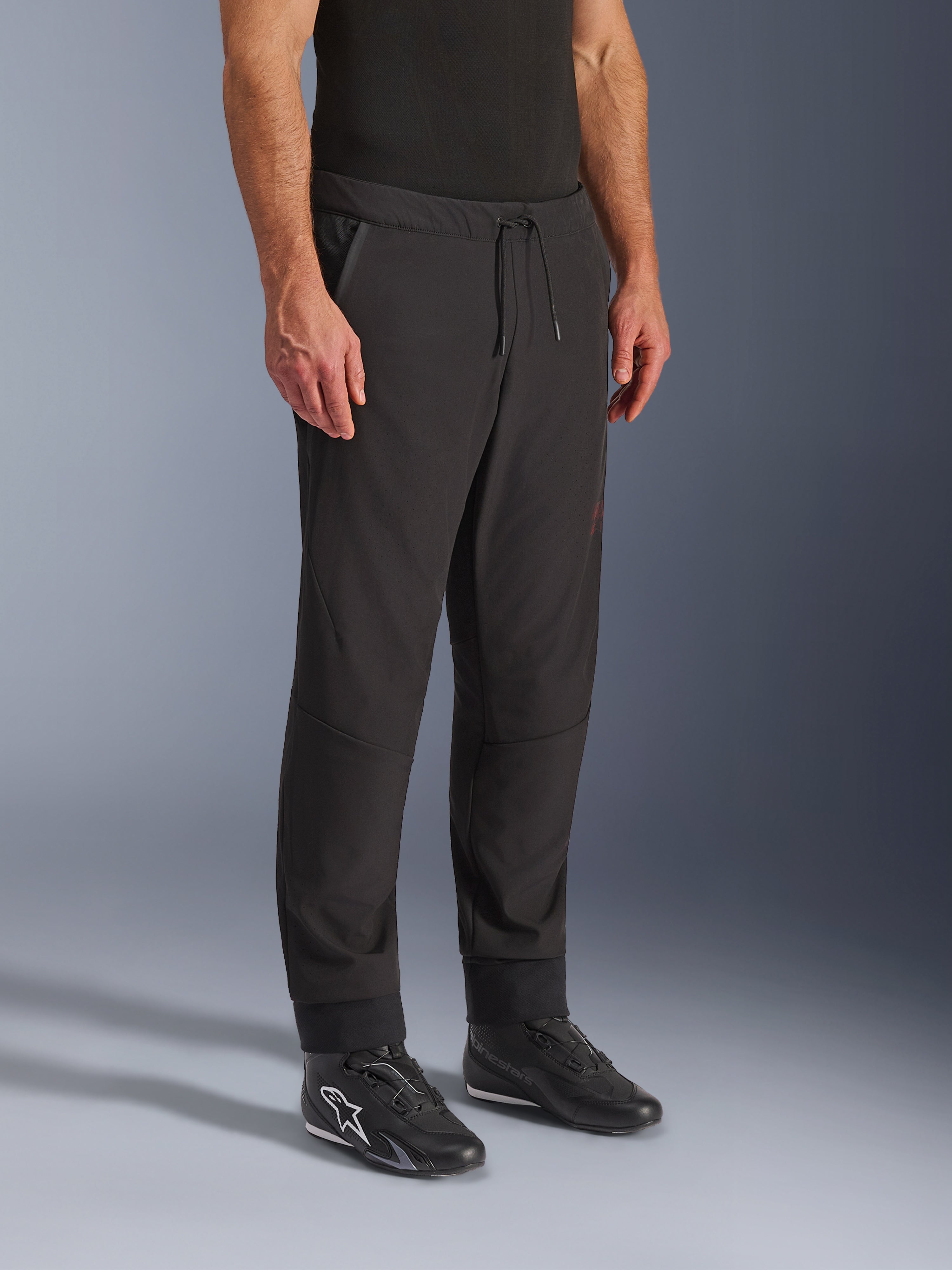 Alpinestars Aeroshell Airflow Pants, Black Motorcycle Pants, worn by model with black riding shoes, featuring a drawstring waistband, cuffed ankles, and laser-perforated softshell fabric for maximum ventilation