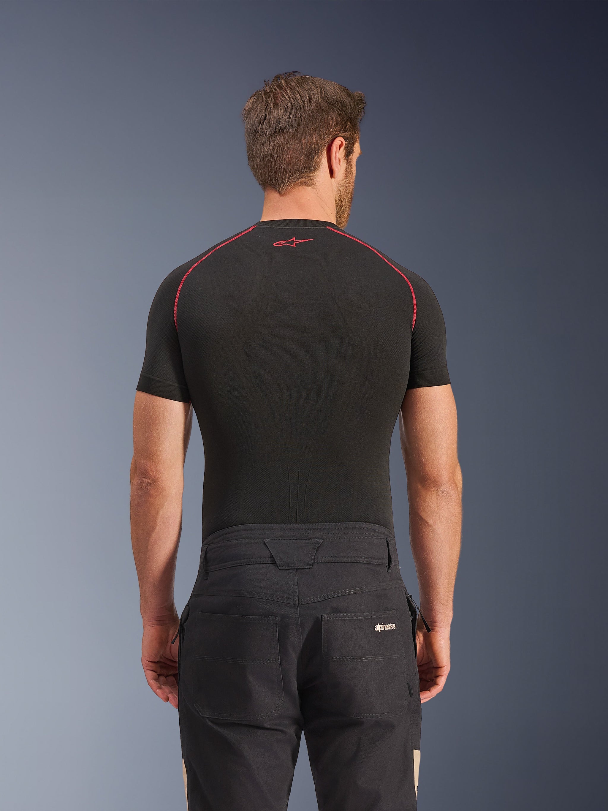 Alpinestars Flex-AST Canvas Pants in Black Aluminum, rear view on model, workwear-inspired urban motorcycle pants with logo on back pocket, paired with a black short-sleeve base layer featuring red stitching.