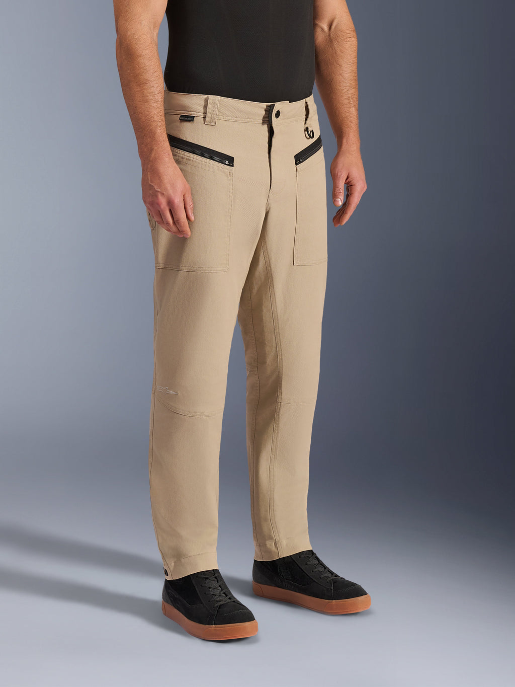 Alpinestars Flex-AST Canvas Pants, Urban Motorcycle Pants, Tan Brown, featuring heritage workwear styling with zippered front pockets and ergonomic knee panels, worn with black sneakers and a black t-shirt, contemporary urban riding gear