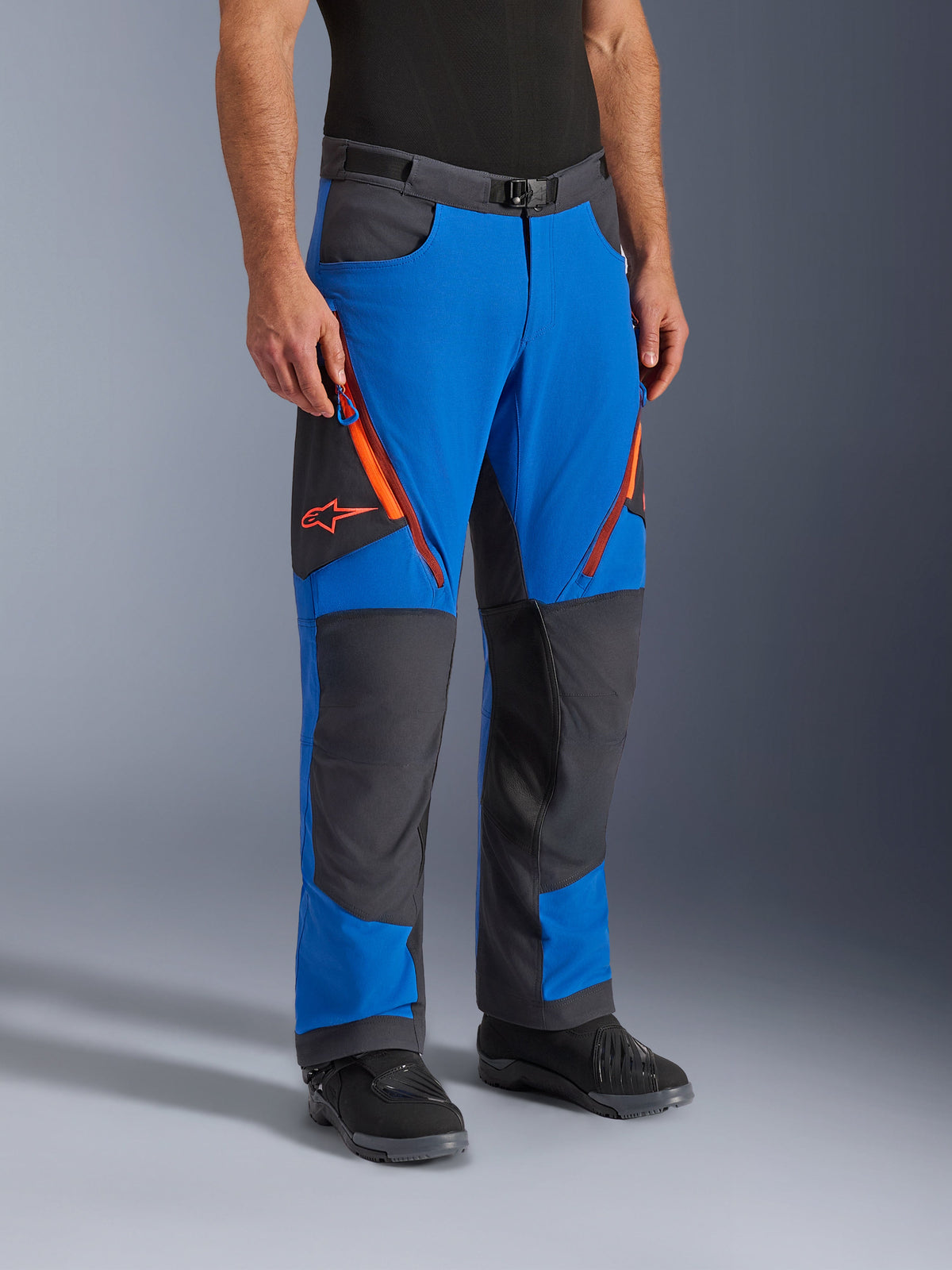 Alpinestars Maxdura Dual Pants, adventure motorcycle pants, Royal Blue and Deep Gray with orange accents, featuring zippered thigh vents, reinforced knee panels, and a magnetic buckle belt, technical over-boot design for dual-sport riding.