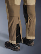 Alpinestars Maxdura Dual Pants in Walnut Aluminum, detailed view of the lower leg and hem featuring an over-the-boot design with adjustable hook-and-loop closures and reinforced inner panels, paired with black motorcycle boots.