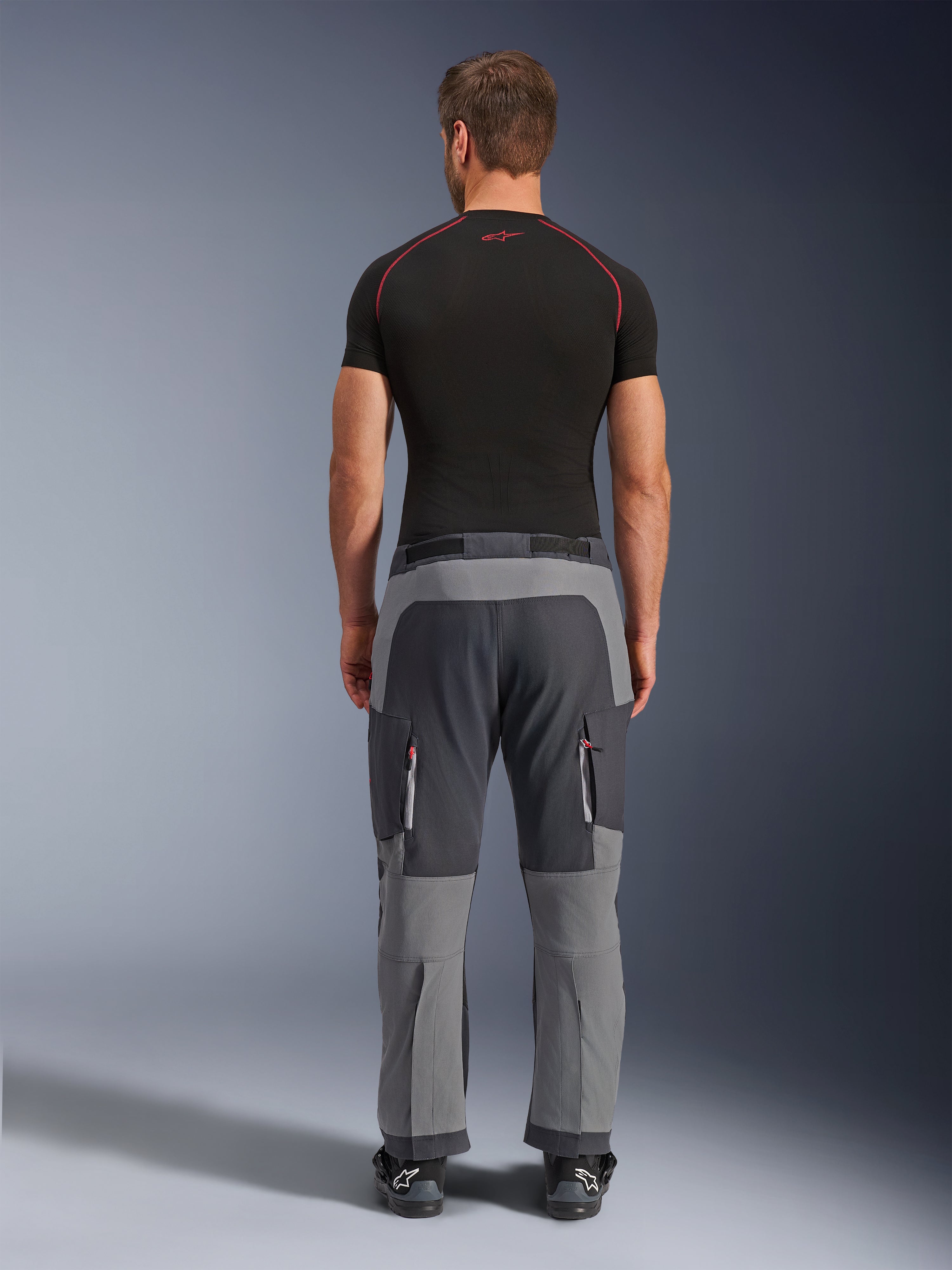 Alpinestars Maxdura Dual Pants, Dark Gray and Deep Gray adventure motorcycle pants, back view on model wearing black t-shirt and boots, featuring multi-tone gray panels and zippered cargo pockets with red accents.