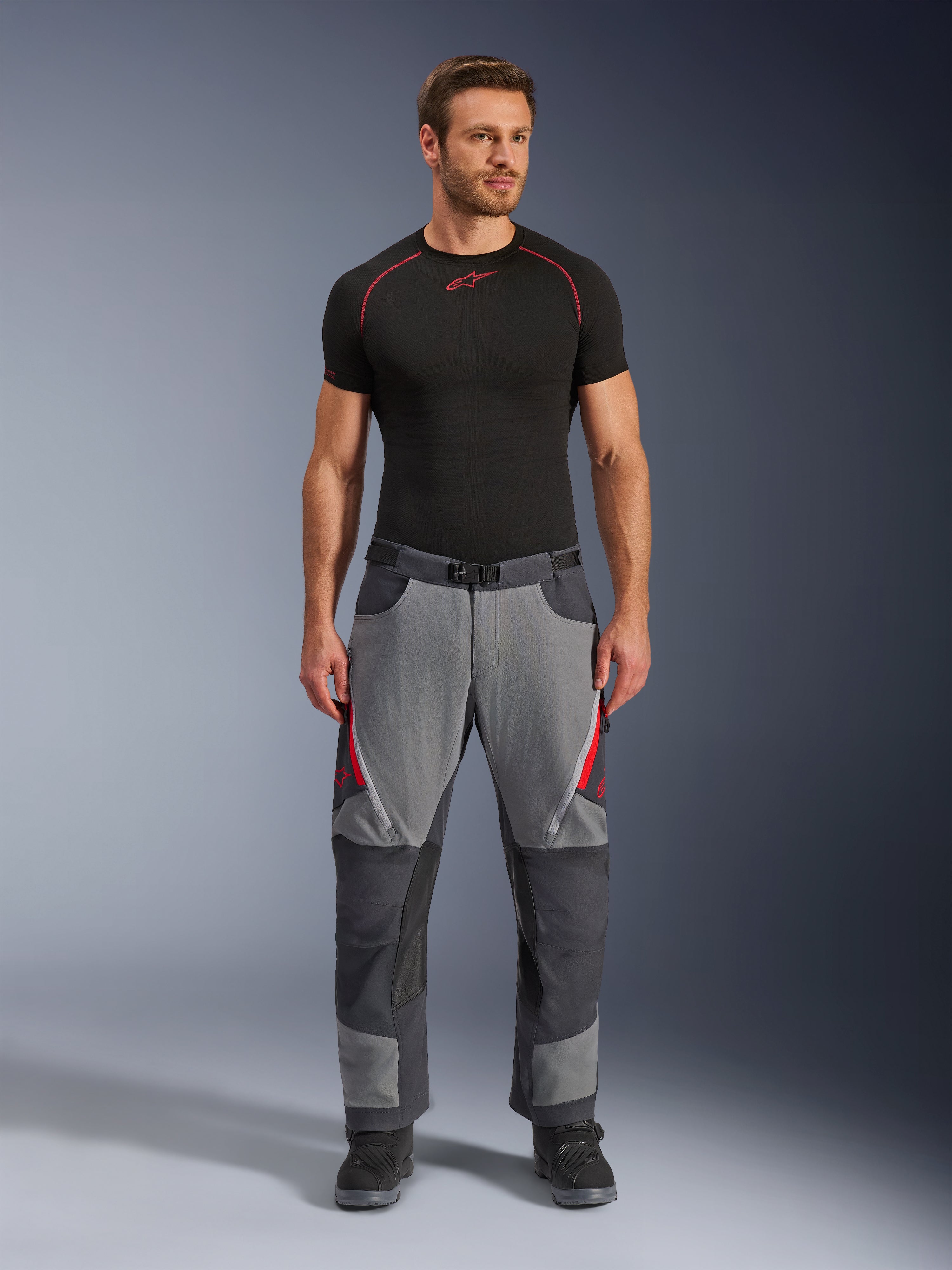 Alpinestars Maxdura Dual Pants, Motorcycle Pants, Dark Gray and Deep Gray with red accents, front view worn by a model with a black Alpinestars base layer and black boots, featuring reinforced panels and zippered thigh vents, adventure-style riding gear