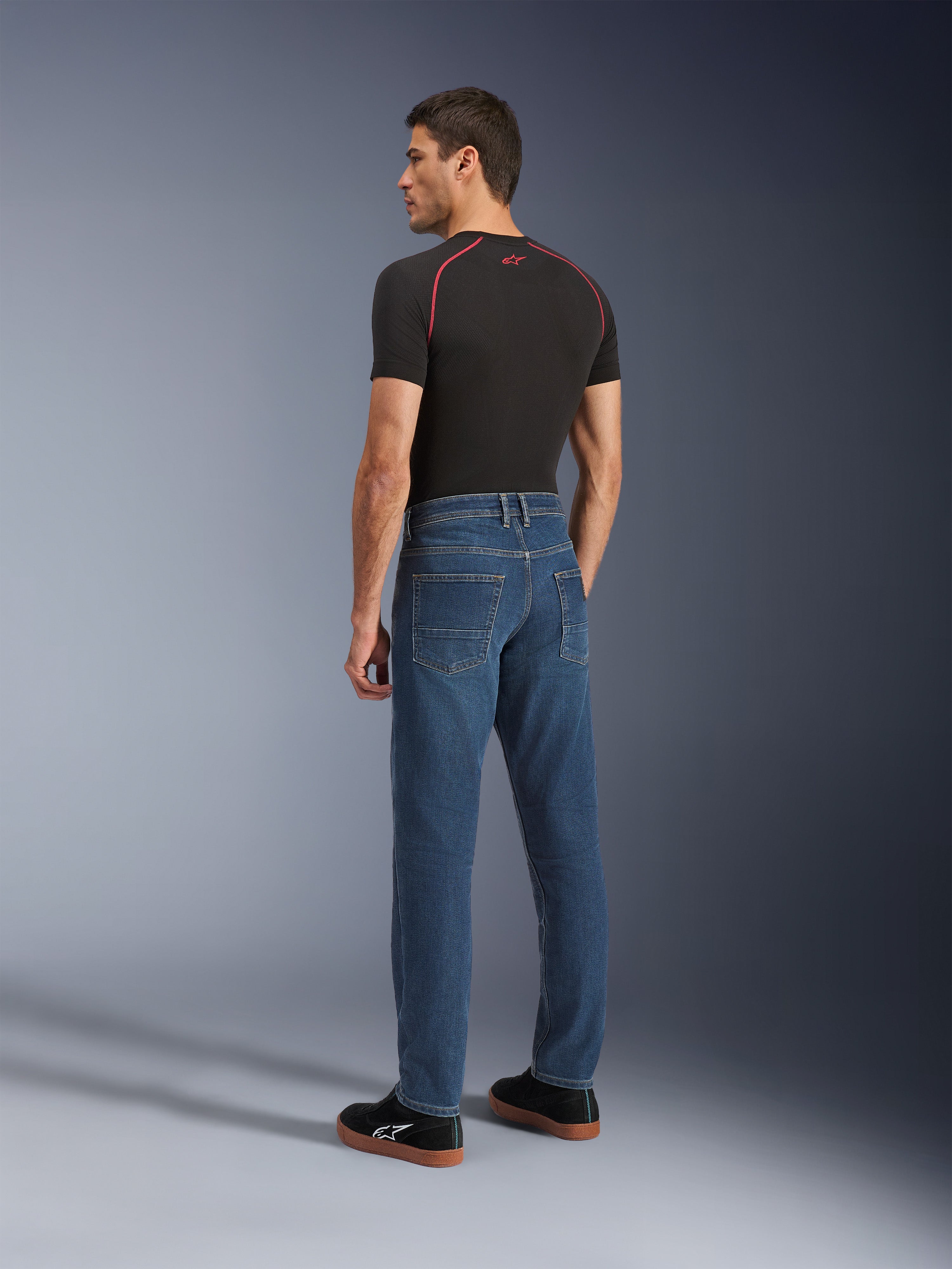 Alpinestars Flex-AST 5 Denim Pants, Indigo Washed, urban motorcycle pants with a tapered fit, shown from the rear on a model wearing a black t-shirt and sneakers, featuring a clean five-pocket design and monolayer stretch construction