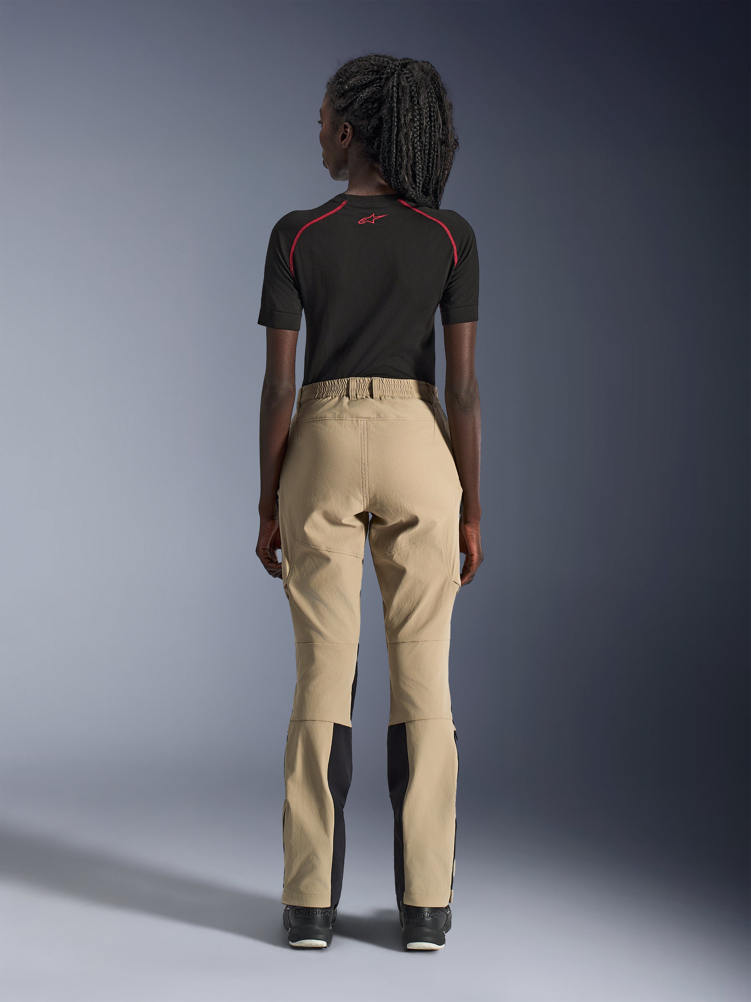 Alpinestars Woman Stella Flex-AST Explorer Pants in Sand, rear view on a model, paired with a black short-sleeved base layer and black boots, featuring reinforced seat panels and ergonomic textile construction for adventure touring.