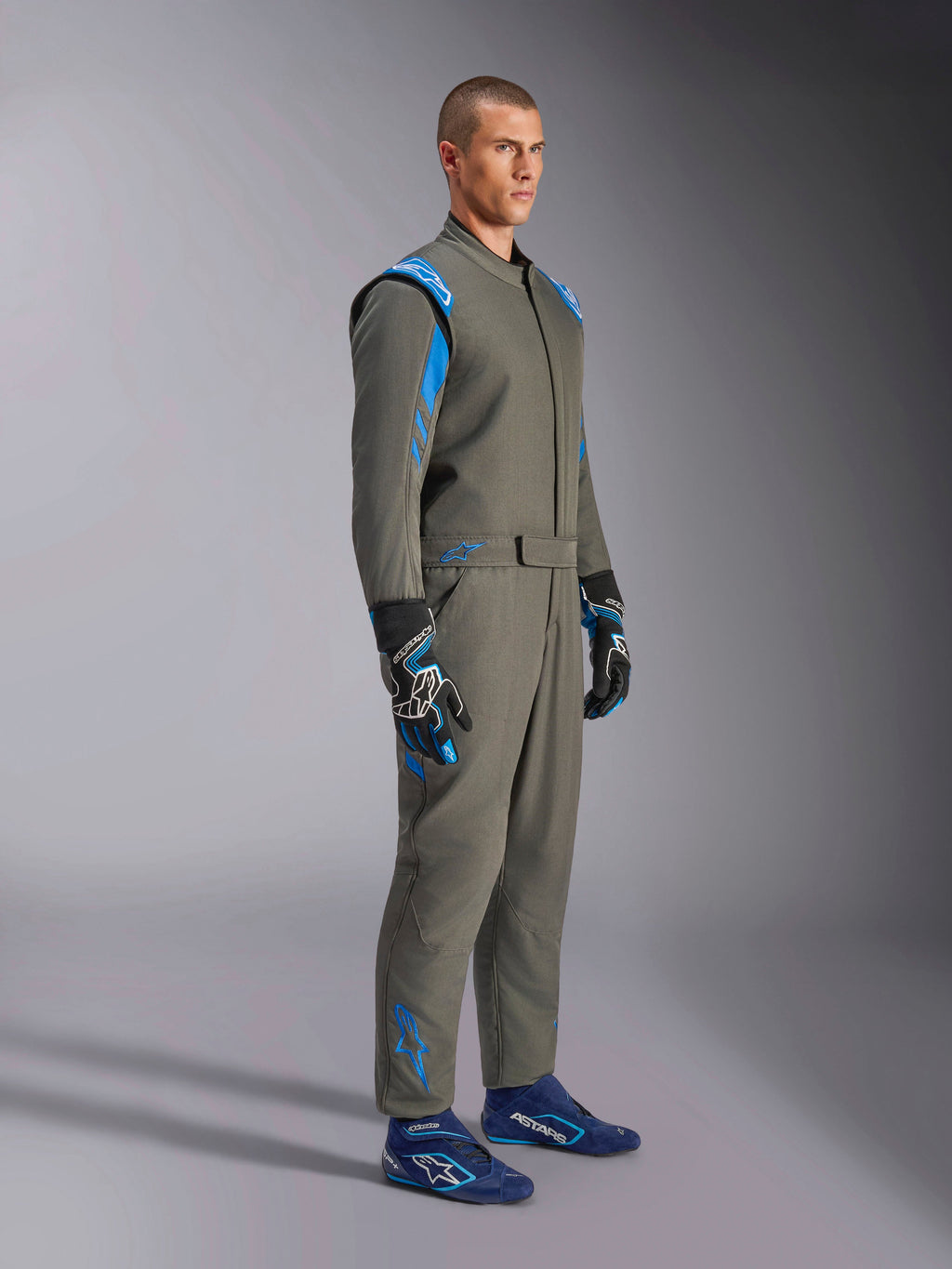 Alpinestars GP Race V3 Suit FIA in Anthracite Blue, one-piece auto racing suit worn by a male model, features bright blue accents on the shoulders and ankles, paired with coordinating racing gloves and blue racing shoes, professional motorsport gear.