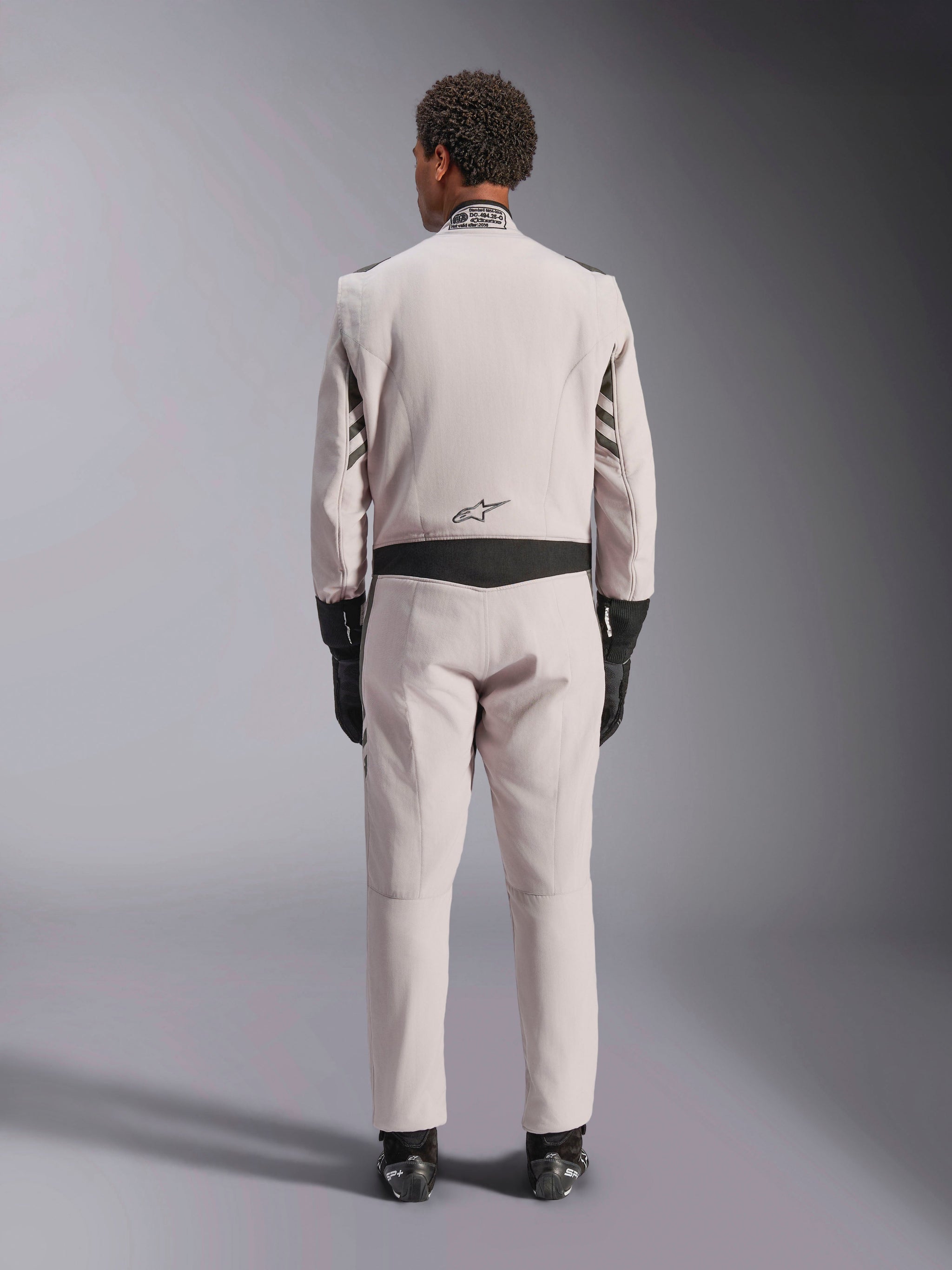 Alpinestars GP Race V3 Suit FIA, Silver Anthracite, back view of one-piece auto racing suit worn with black gloves and boots, featuring black stretch panels on the waist and sleeves, professional motorsport design