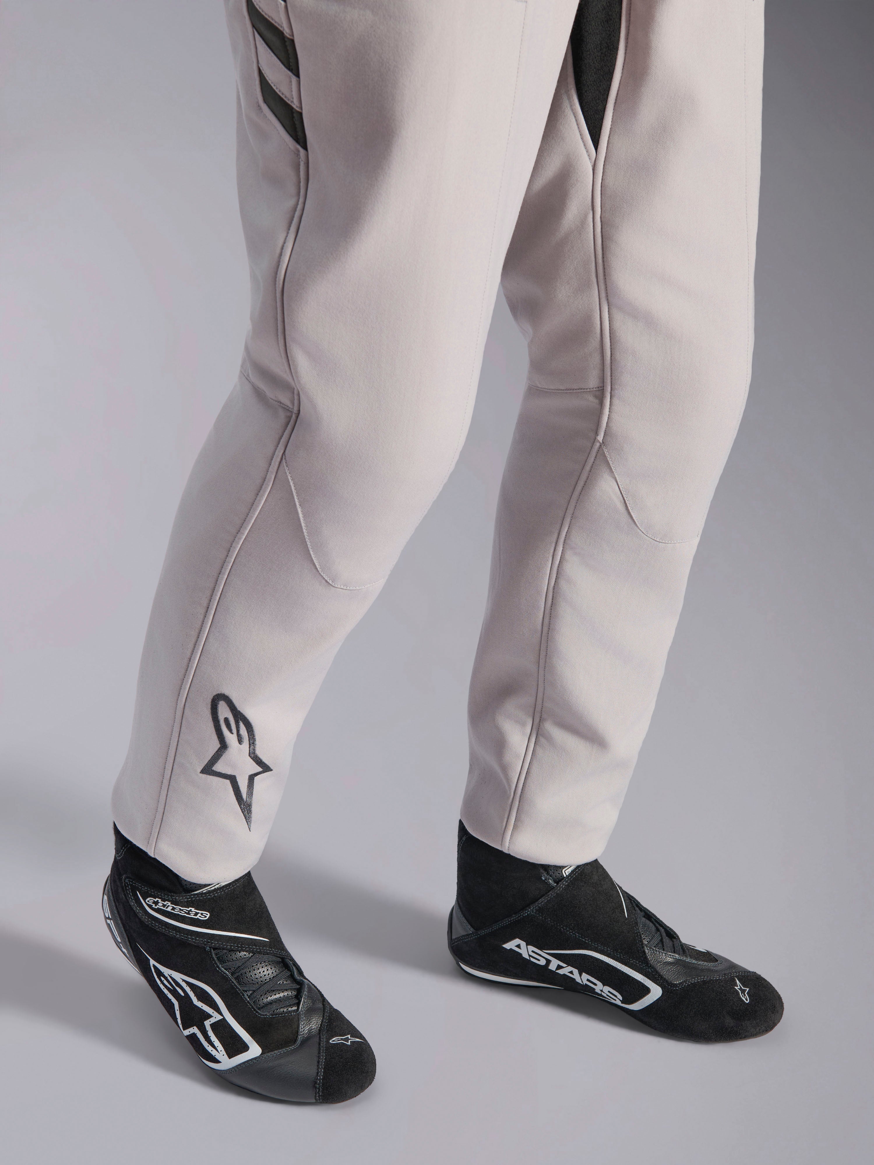 Alpinestars GP Race V3 Suit FIA, Silver Anthracite auto racing suit, detail shot of lower legs and black racing boots, featuring the black Astars logo on the calf, professional motorsport gear with ribbed cuffs