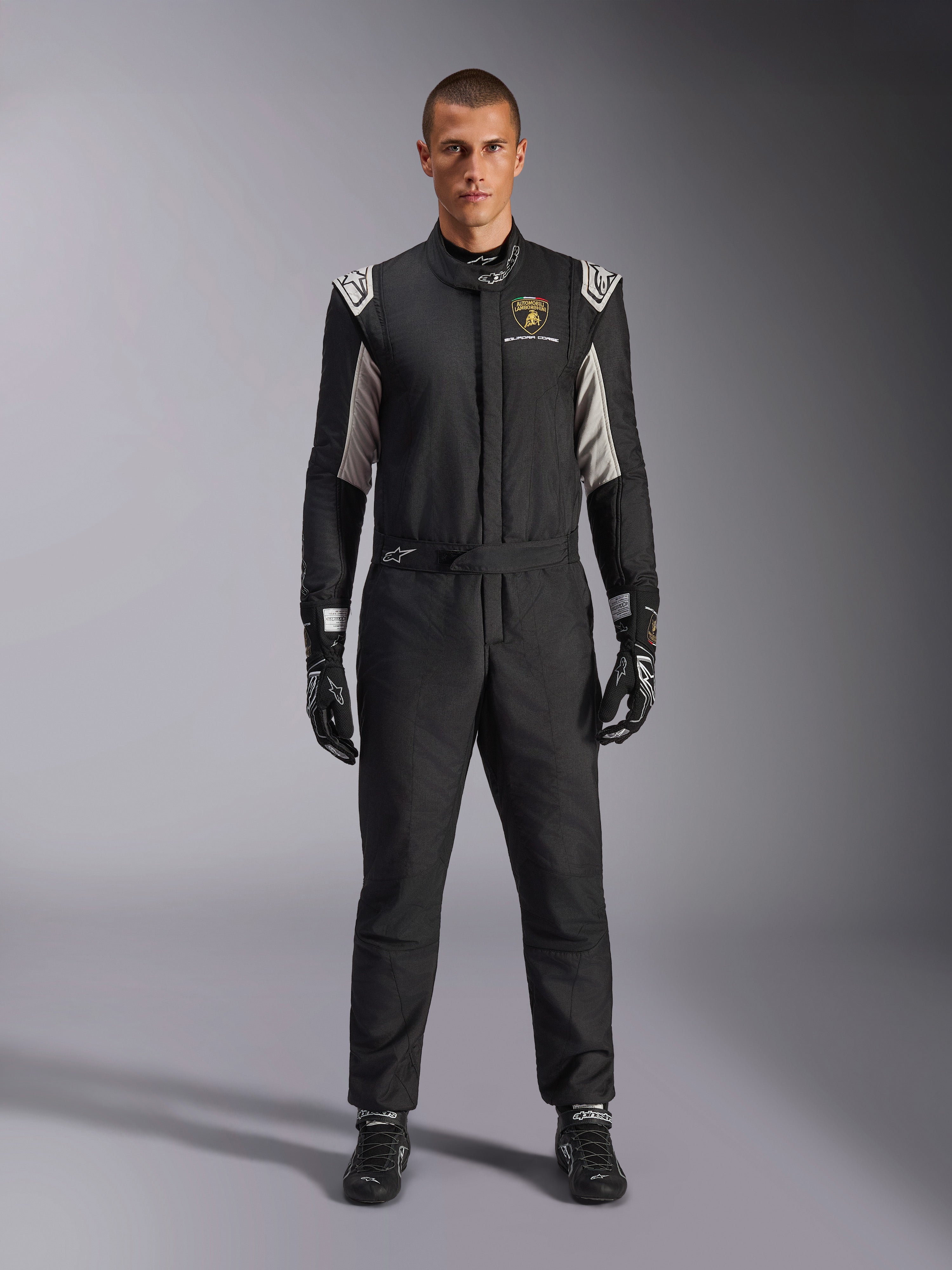 Alpinestars Limited Edition Lamborghini GP Tech V4 Suit FIA, professional auto racing suit, Black with Silver and Gold accents, featuring Automobili Lamborghini Squadra Corse logo on chest, worn with matching racing gloves and boots, sleek athletic design for circuit competition