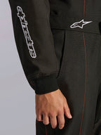 Close-up of Alpinestars KMX-9 V3 Suit in Black and Red Fluo, featuring white embroidered Alpinestars branding on the sleeve, a knitted wrist cuff, and a waist belt with the Astars logo and red contrast stitching.