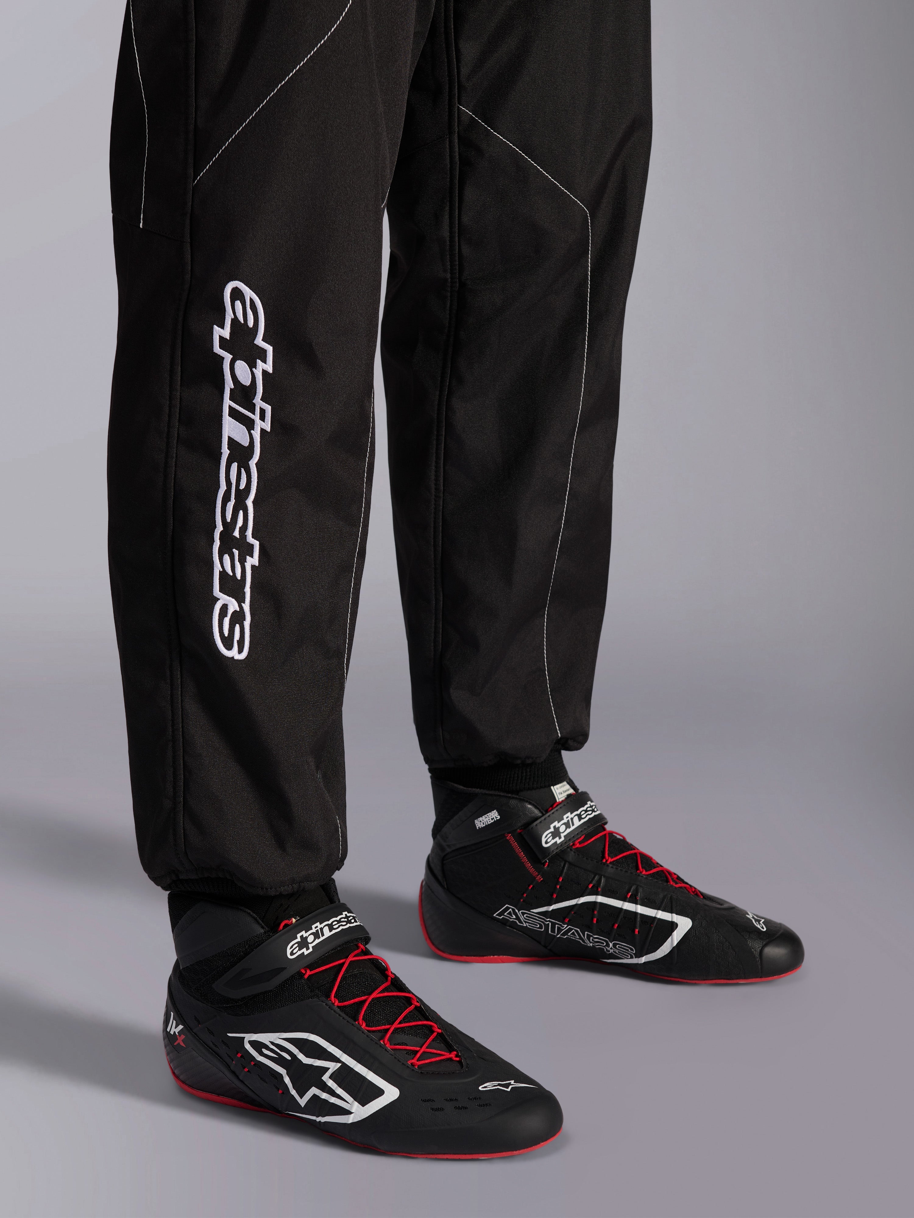 Alpinestars KMX-9 V3 Suit, Karting Suit, Black and White, lower leg view showing large white Alpinestars branding, worn with black and red racing boots, professional motorsport gear for karting