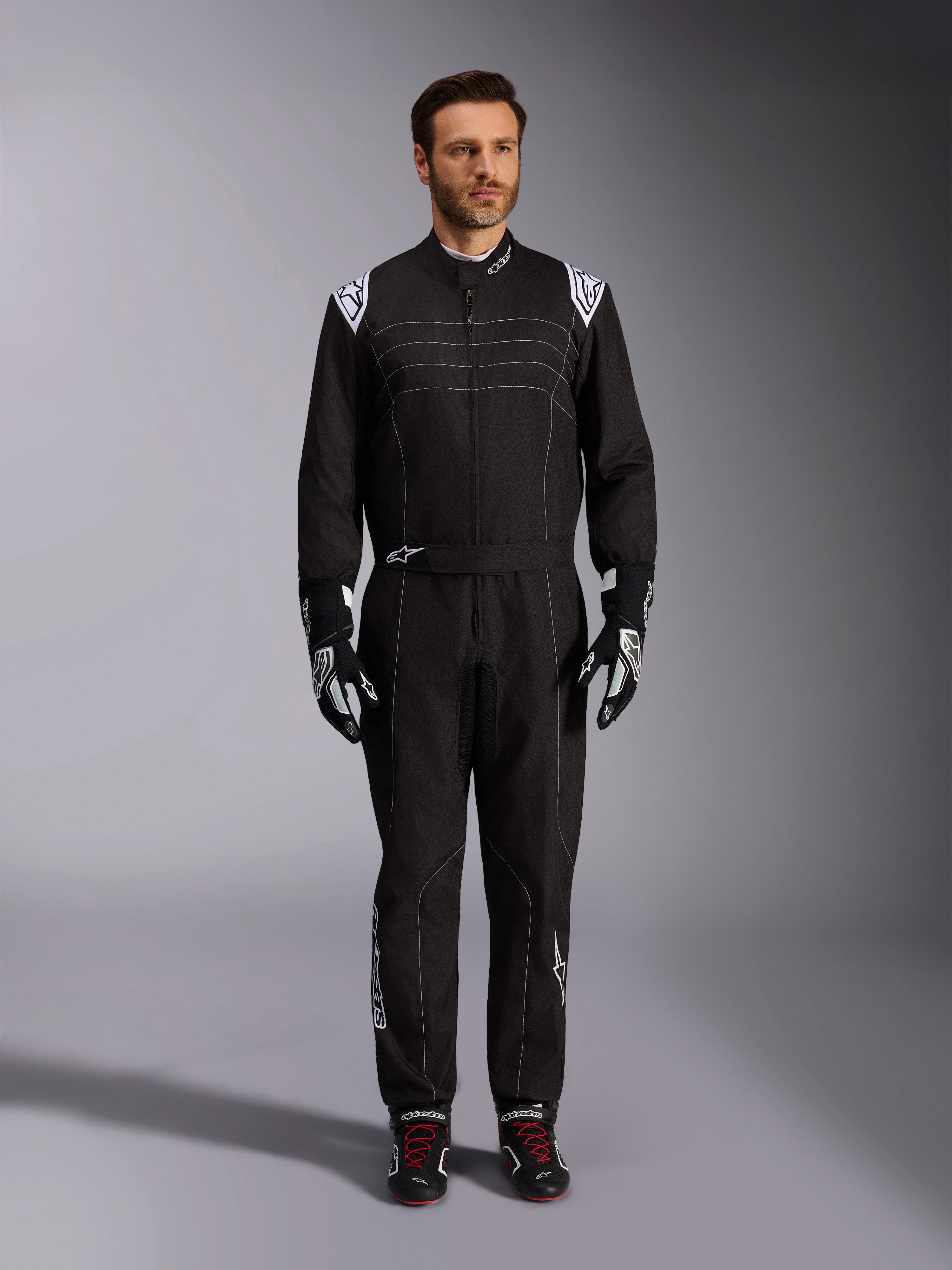 Alpinestars KMX-9 V3 Suit, Black and White Karting Suit, full-length view on a model, featuring white shoulder logos and accents, styled with black and white racing gloves and black shoes with red laces, athletic-regular fit for professional karting gear.