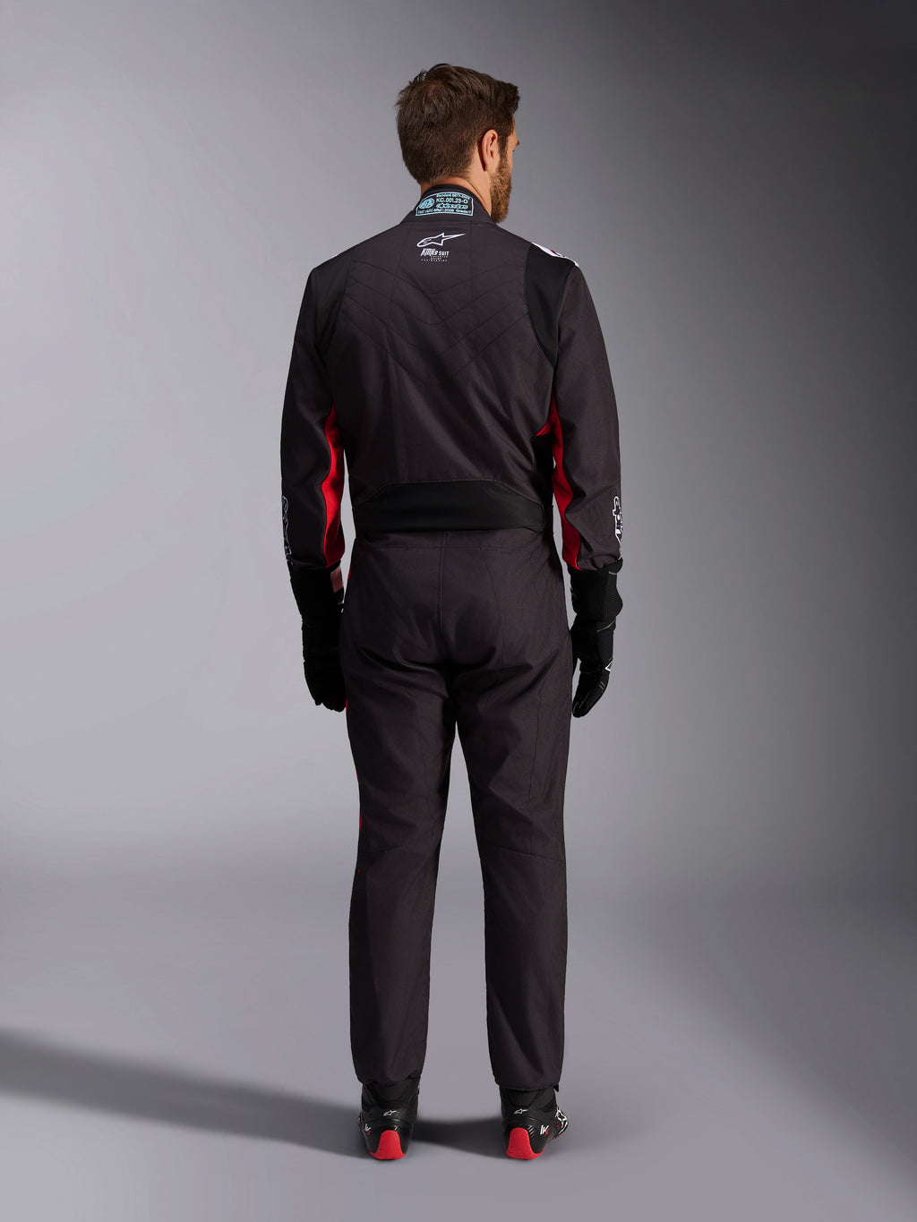 Alpinestars KMX-9 V3 Graphic 3 Suit, Karting Suit, Black and Red, rear view featuring the lumbar stretch panel and FIA certification tag on the collar, styled with black racing gloves and red-accented boots