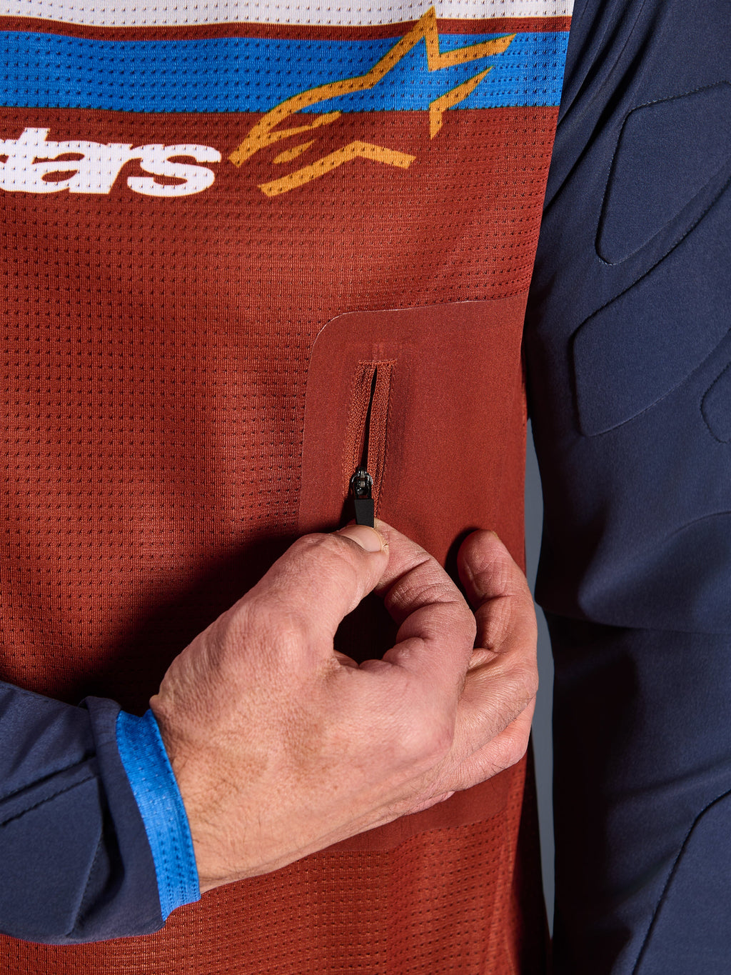 Close-up of Alpinestars Maxdura Dual Jersey, Rust Brown mesh torso with seamless zippered chest pocket, Mood Indigo sleeves with integrated padding, technical adventure motorcycle jersey detail